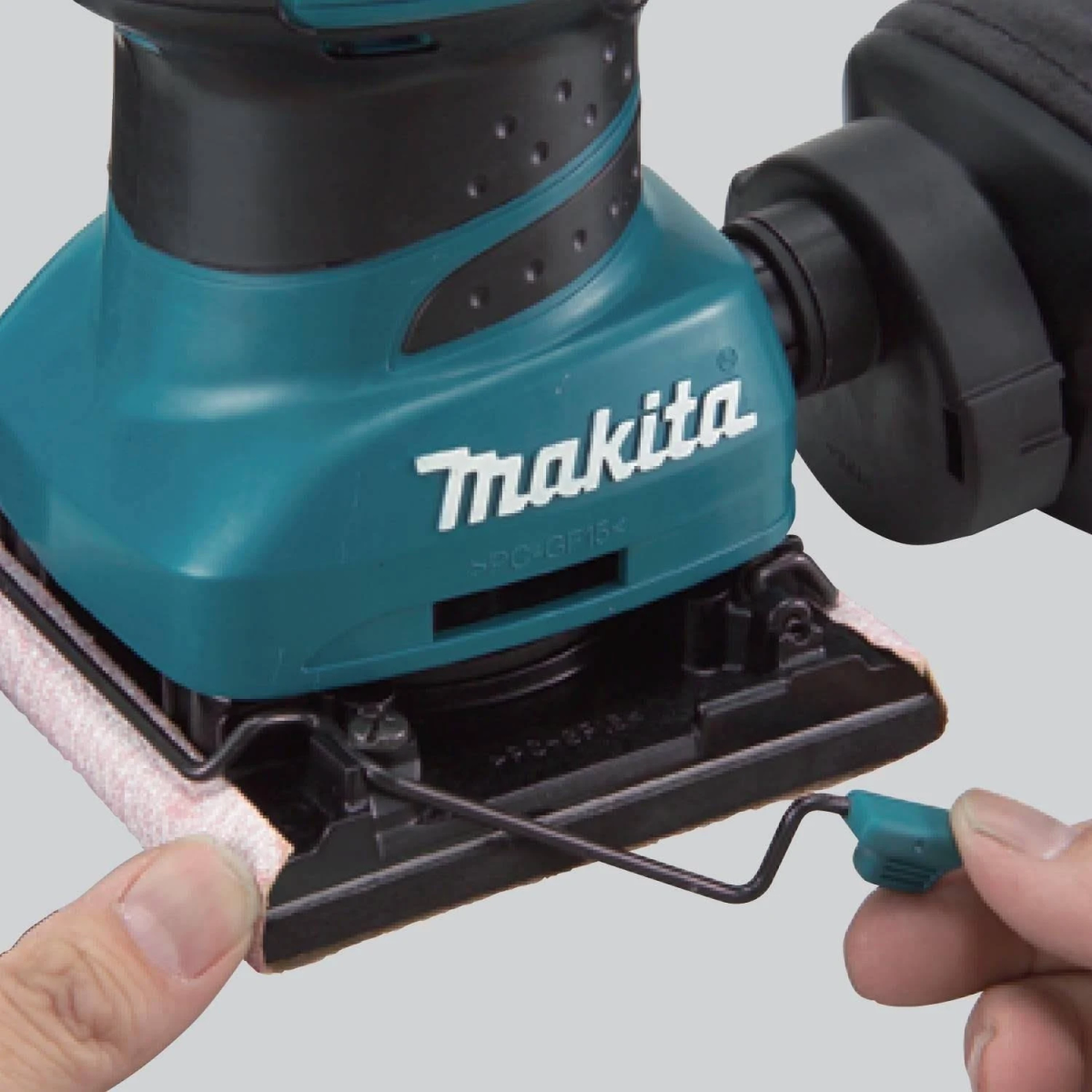 Primer plano de una lijadora Makita turquesa, que muestra la almohadilla de lijado y el dedo de una mano.