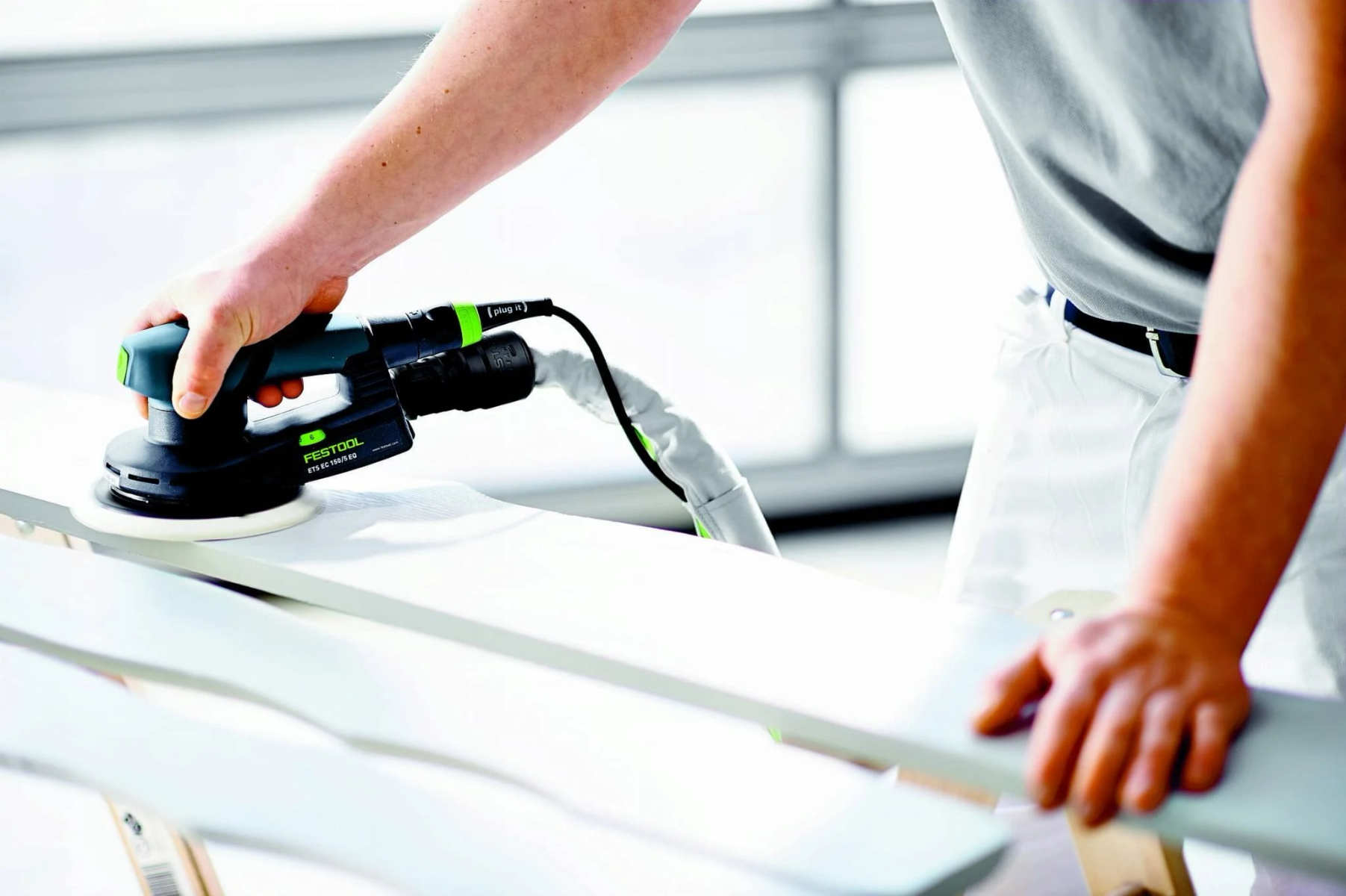 Una persona lijando una tabla de madera con una lijadora Festool, en un taller.