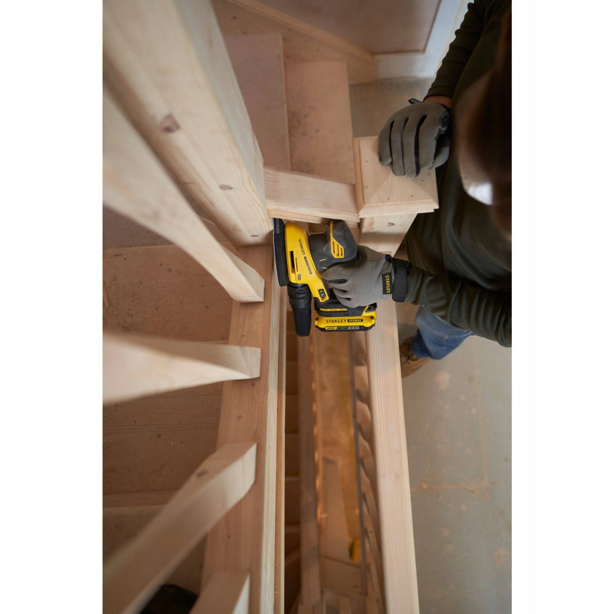Persona lijando barandilla de escalera de madera con lijadora Stanley amarilla y negra.