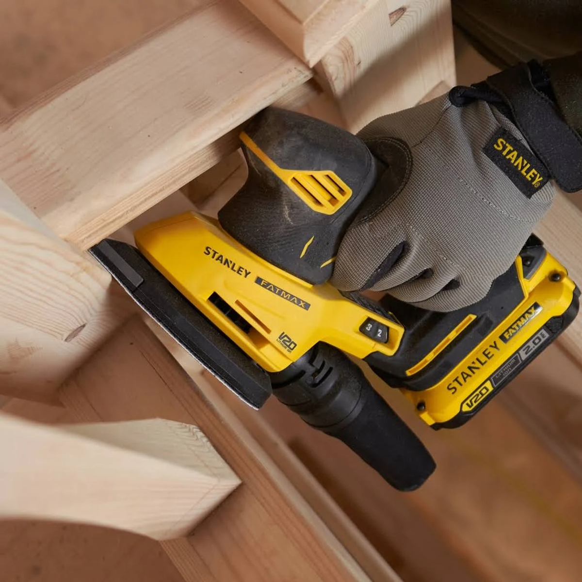 Una lijadora Stanley FatMax amarilla y negra que se utiliza en una estructura de madera con una mano enguantada.