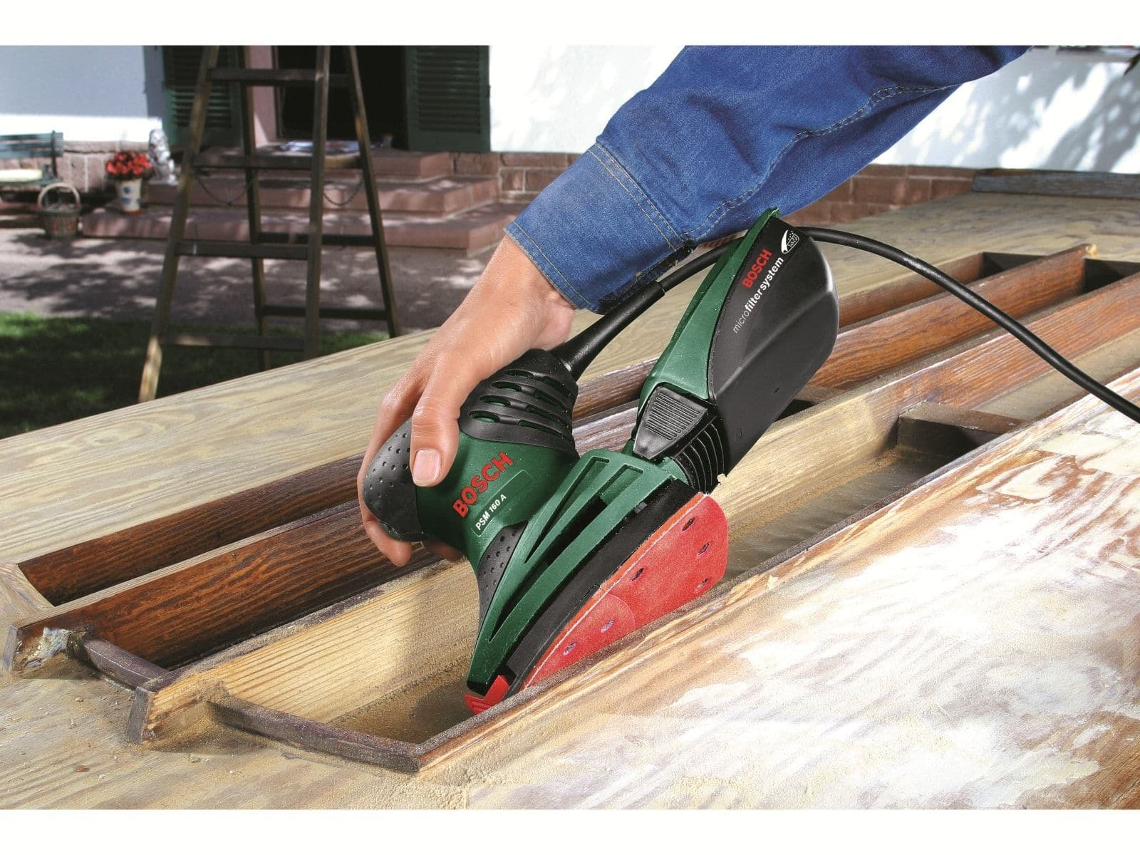Une personne utilise une ponceuse sur une surface en bois, vue de près.