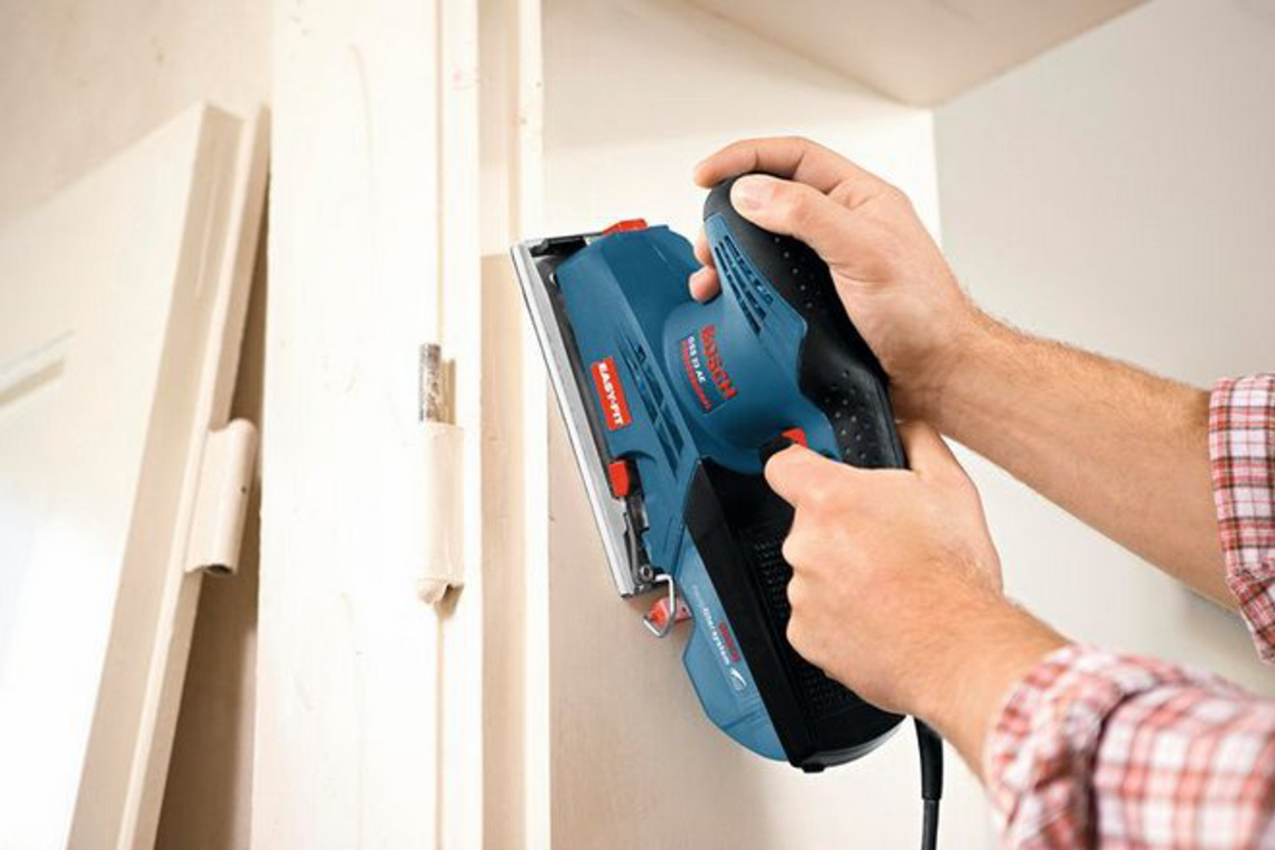 Una persona usando una lijadora Bosch azul y negra en una puerta blanca, lijando la madera.