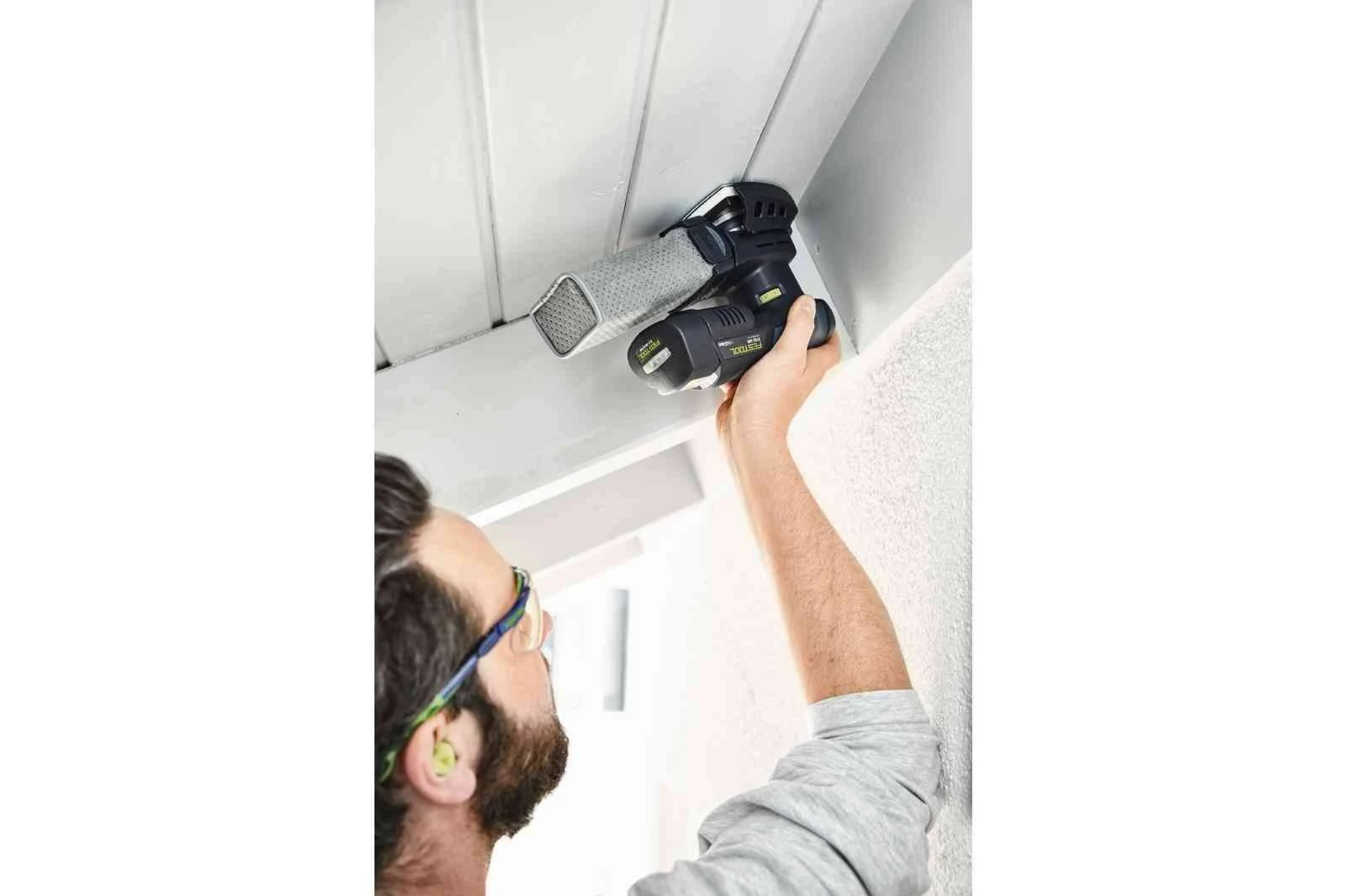 Un uomo usa una levigatrice su una superficie bianca. L'utensile è attaccato al soffitto.