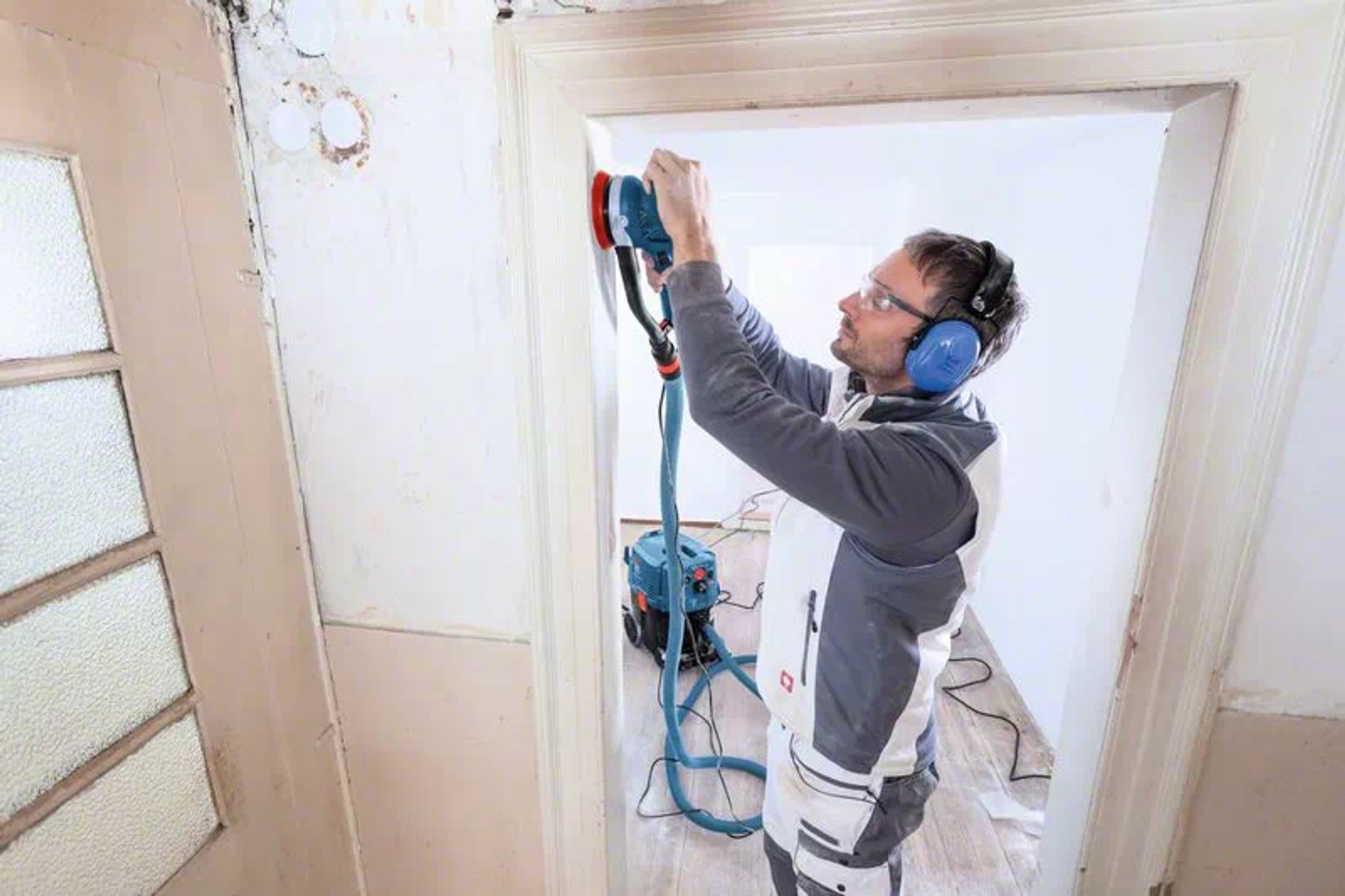 Una persona lijando un marco de puerta con una lijadora, usando protección auditiva.