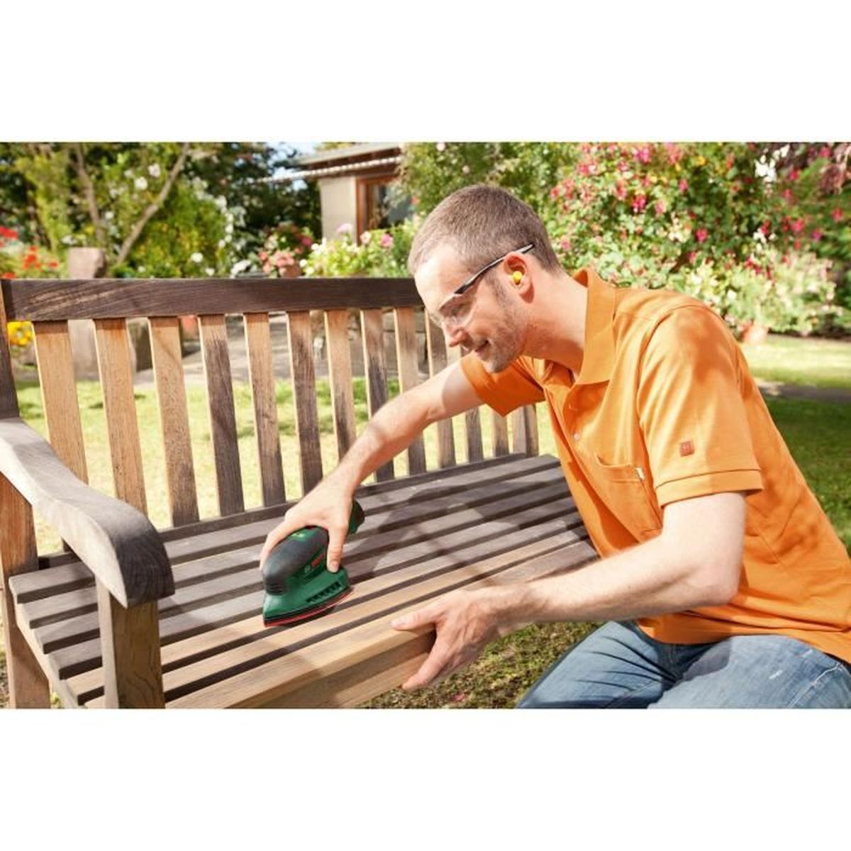 Homme ponçant un banc en bois avec une ponceuse électrique à l'extérieur.