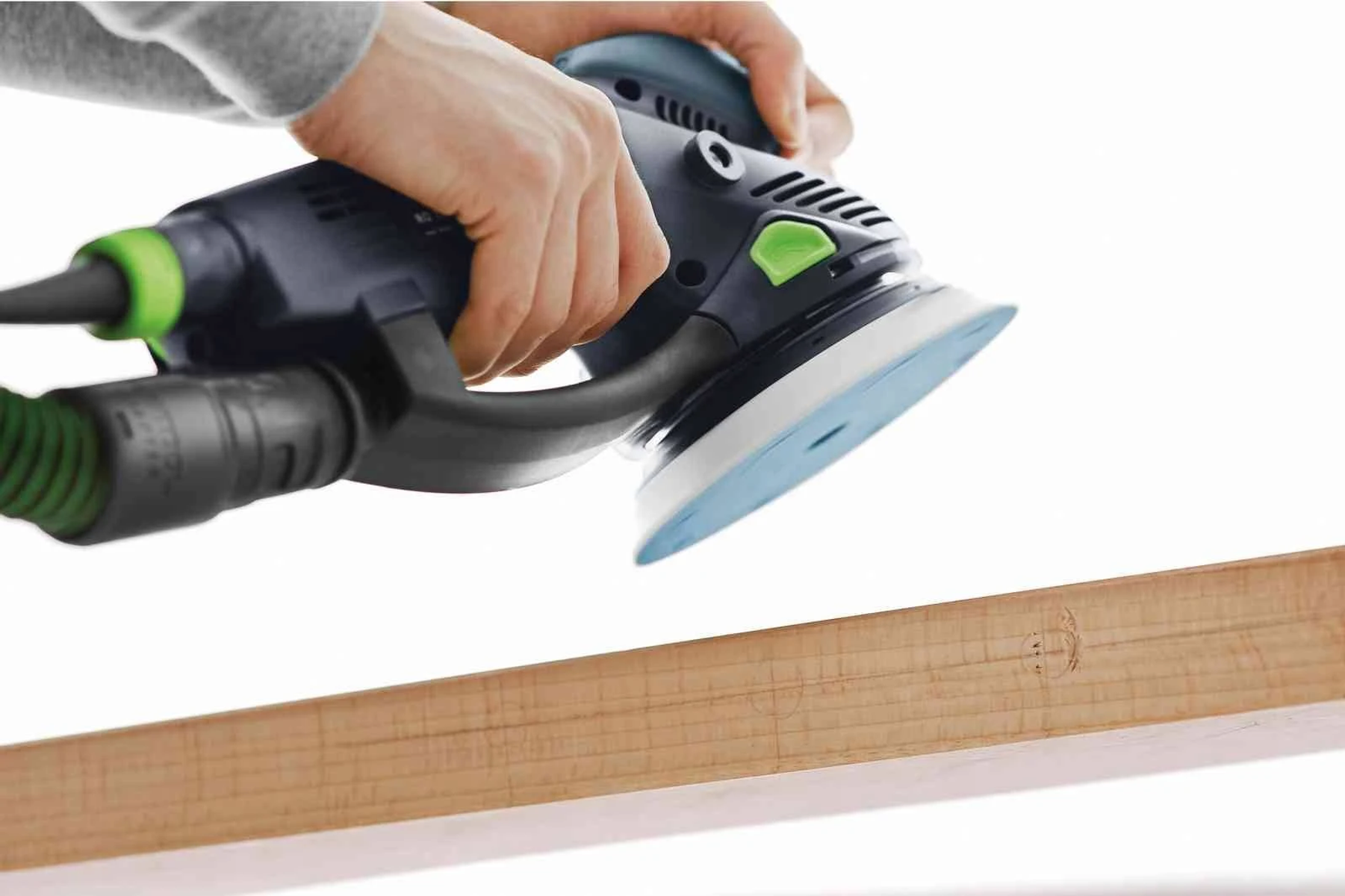 Una persona lija una tabla de madera con una lijadora Festool; fondo blanco.