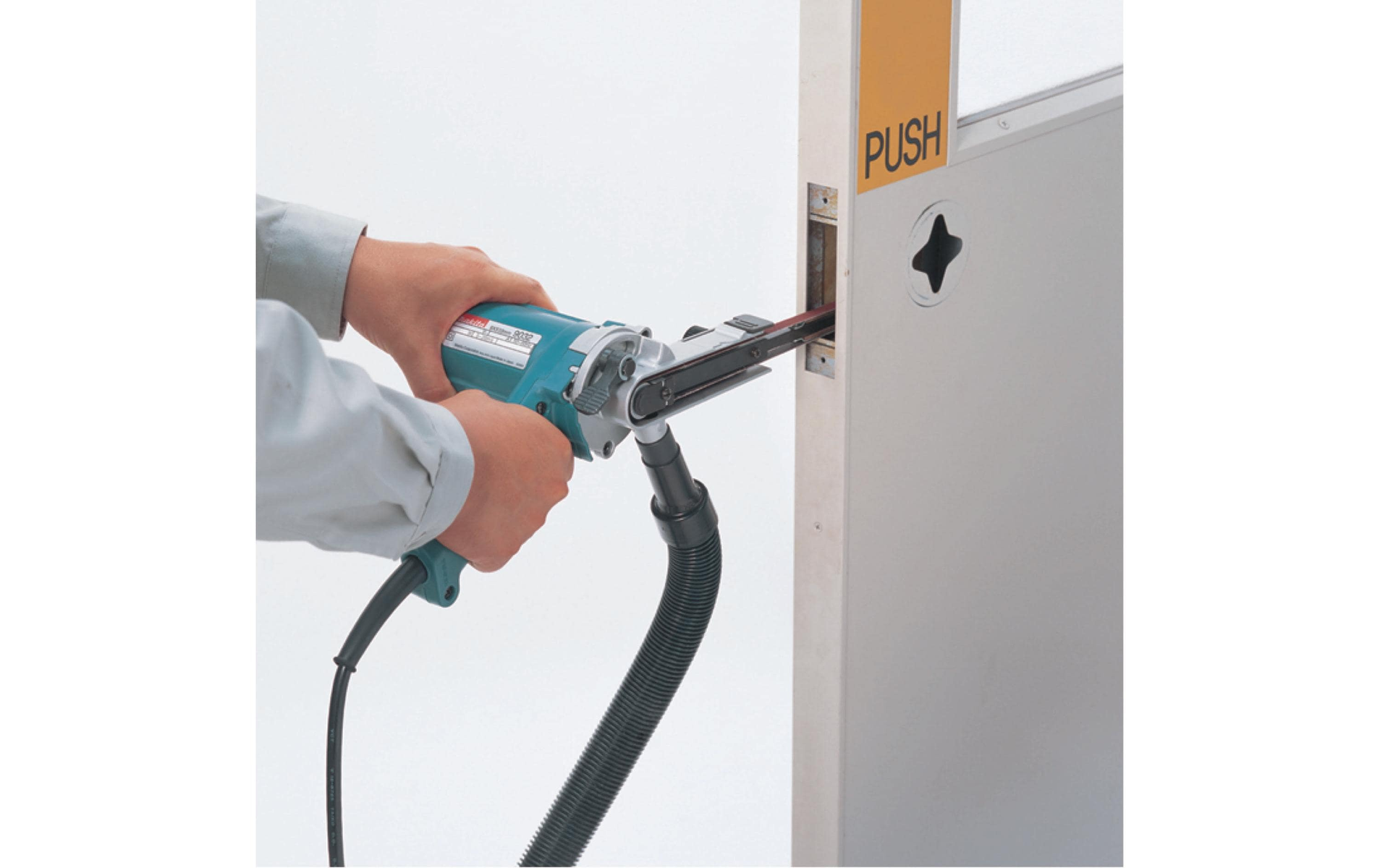 Personne utilisant une ponceuse à bande Makita pour poncer un cadre de porte, avec un aspirateur attaché.