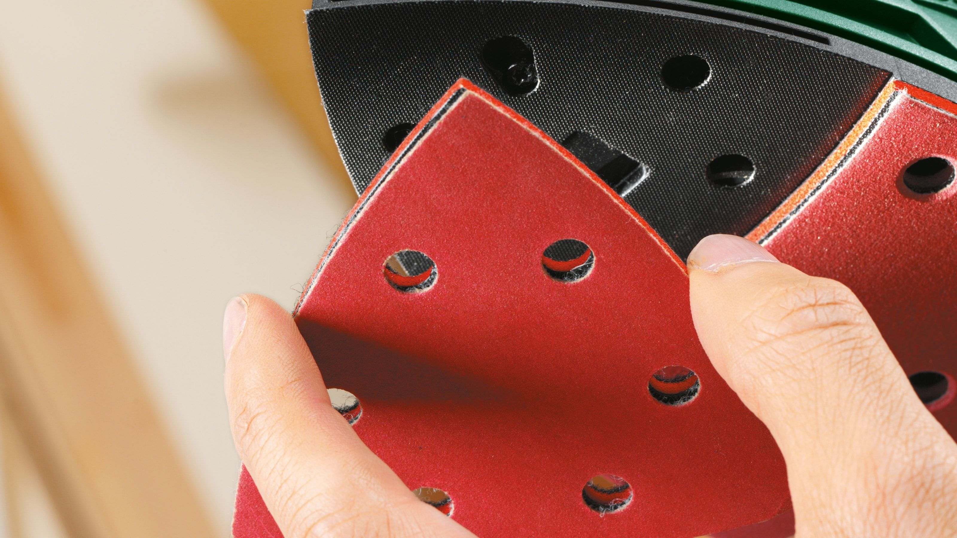 Main tenant du papier de verre triangulaire rouge. Le fond est une ponceuse.