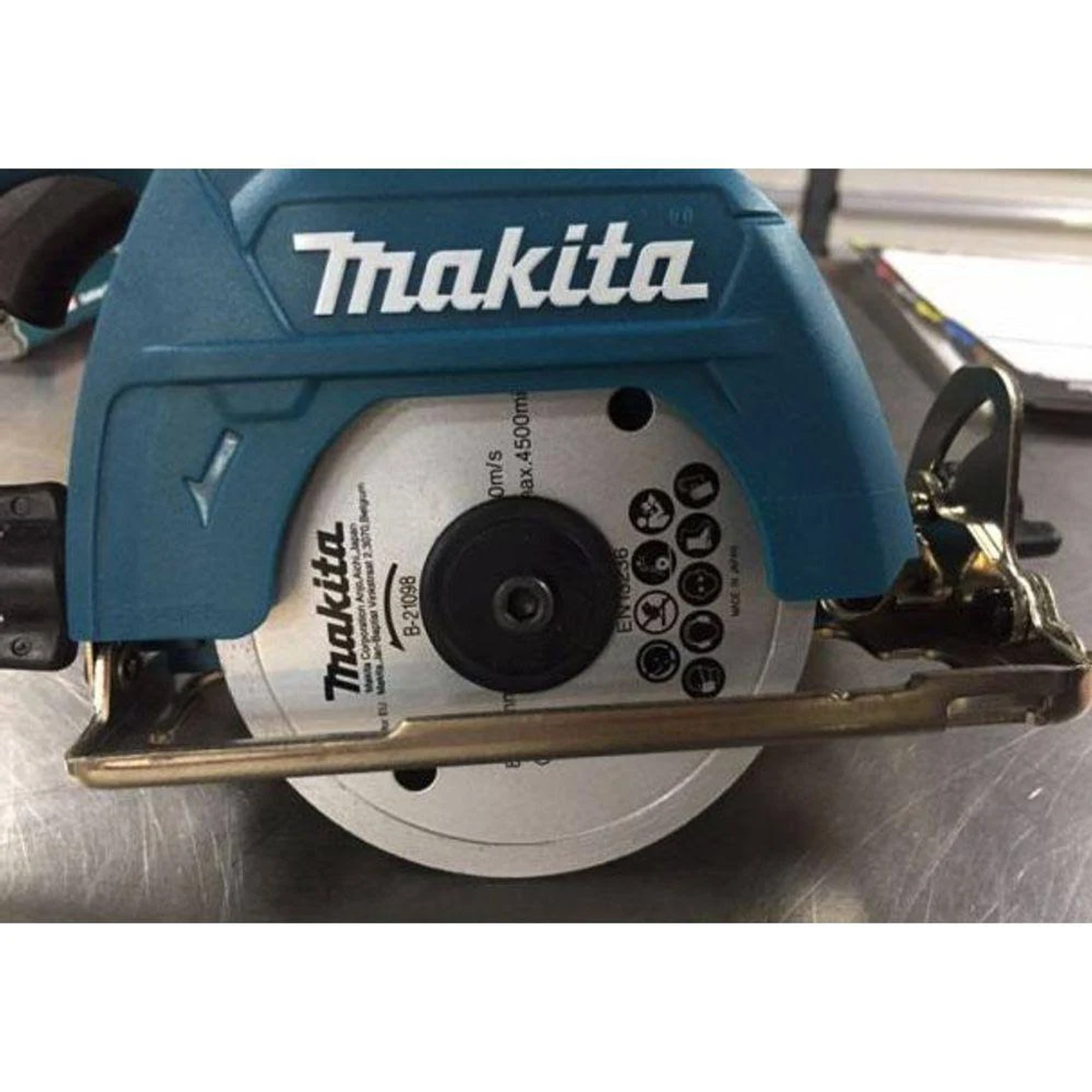 Una sierra circular Makita turquesa. Hoja expuesta, con base plateada, sobre superficie metálica.