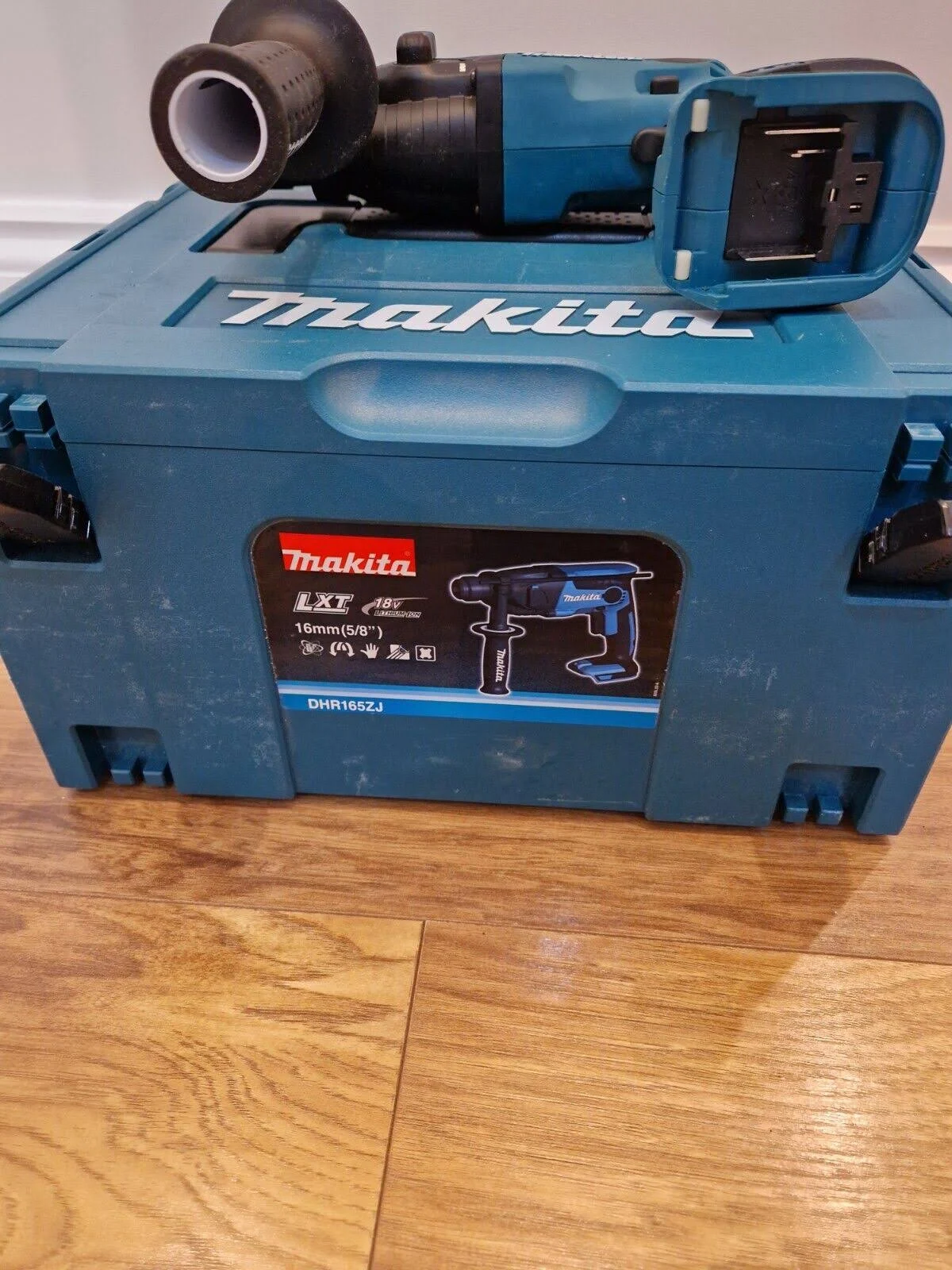 Caja de herramientas Makita turquesa con taladro y batería turquesa, en suelo de madera. Taladro fuera.
