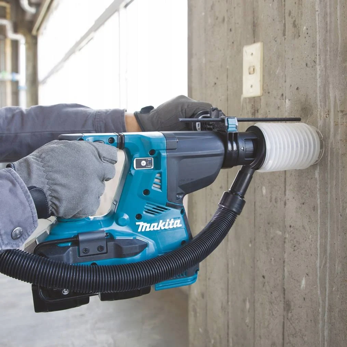 Persona usando taladro Makita para perforar pared de concreto con manguera de vacío.