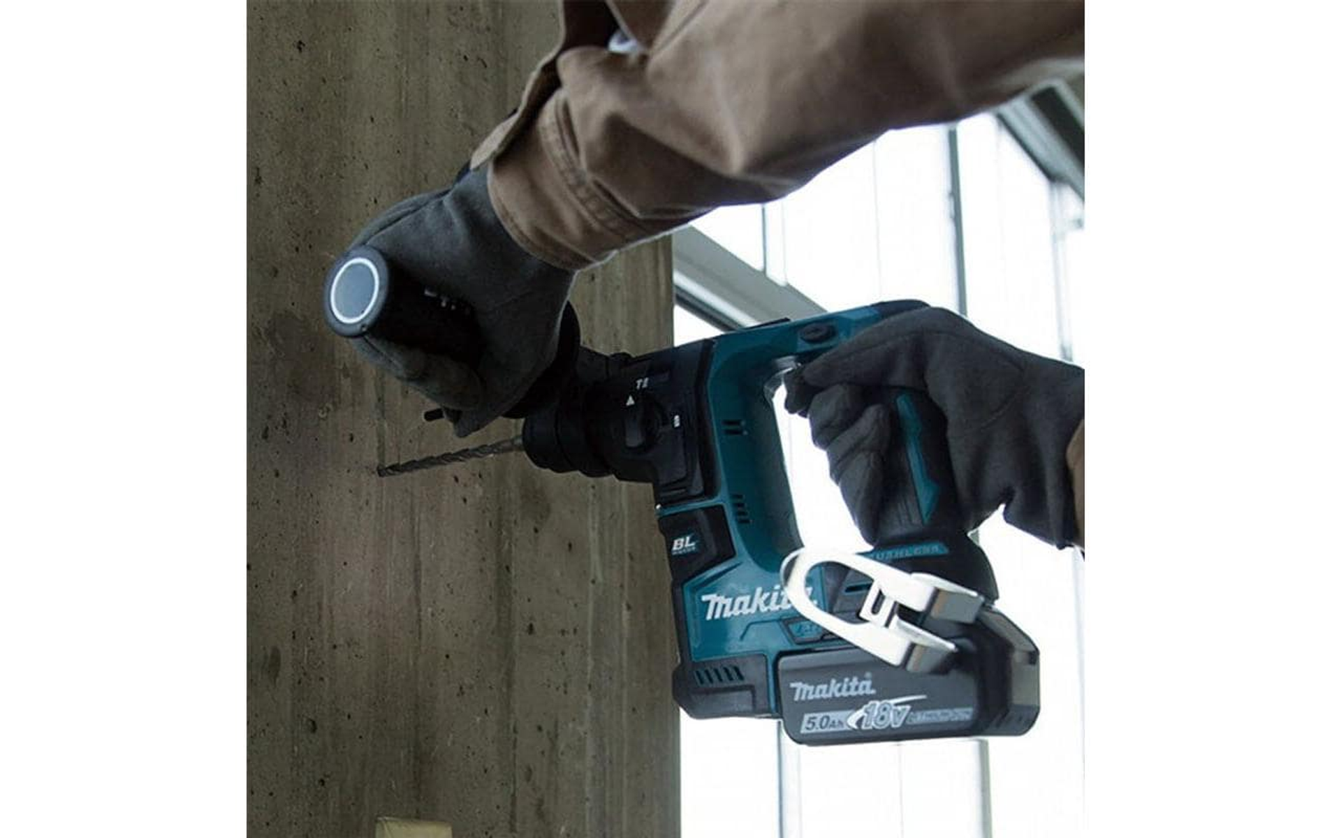 Hand, die eine Makita-Bohrmaschine hält und in eine Betonwand bohrt.
