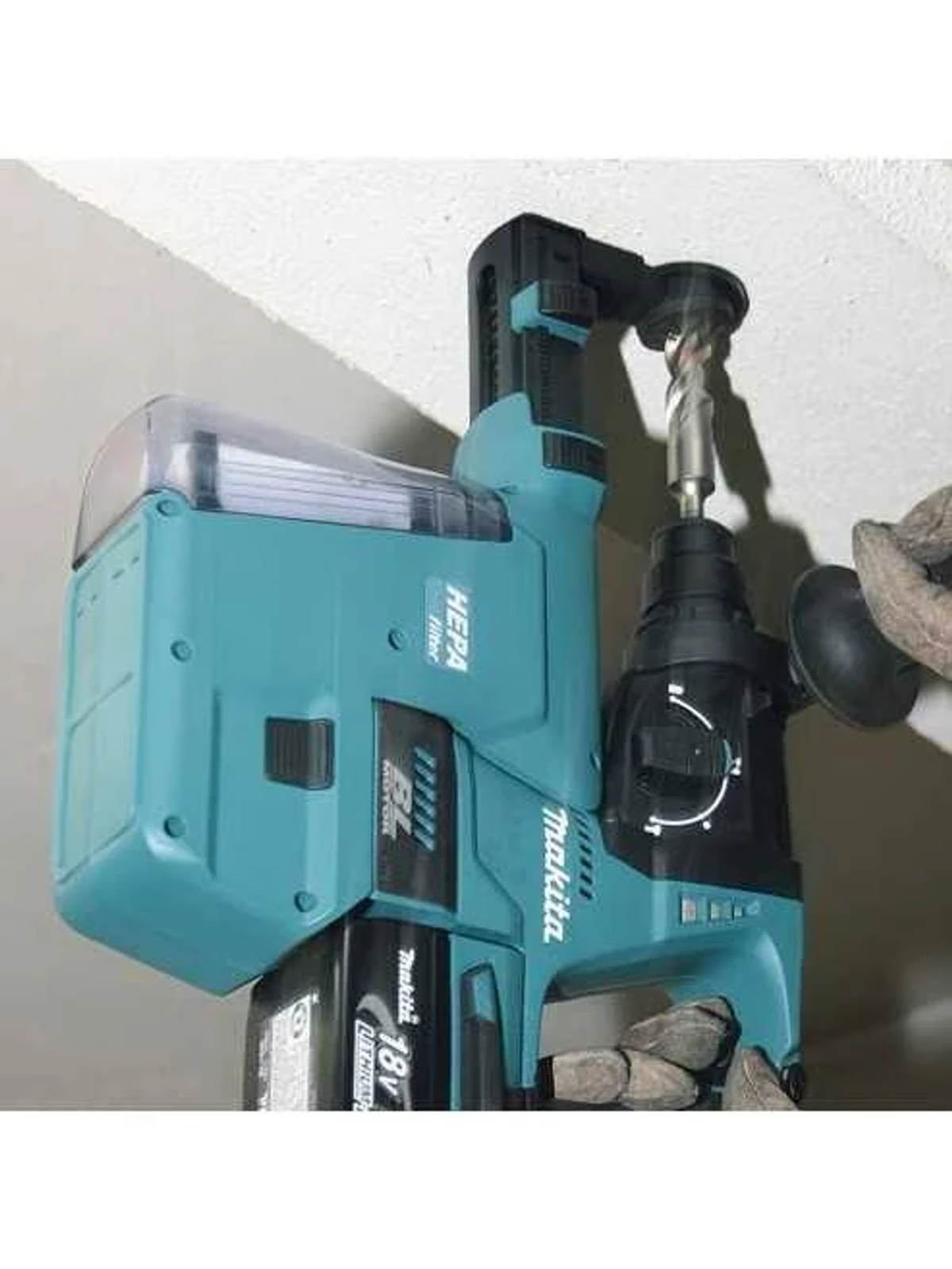 Un taladro Makita turquesa con un colector de polvo se usa en un techo.