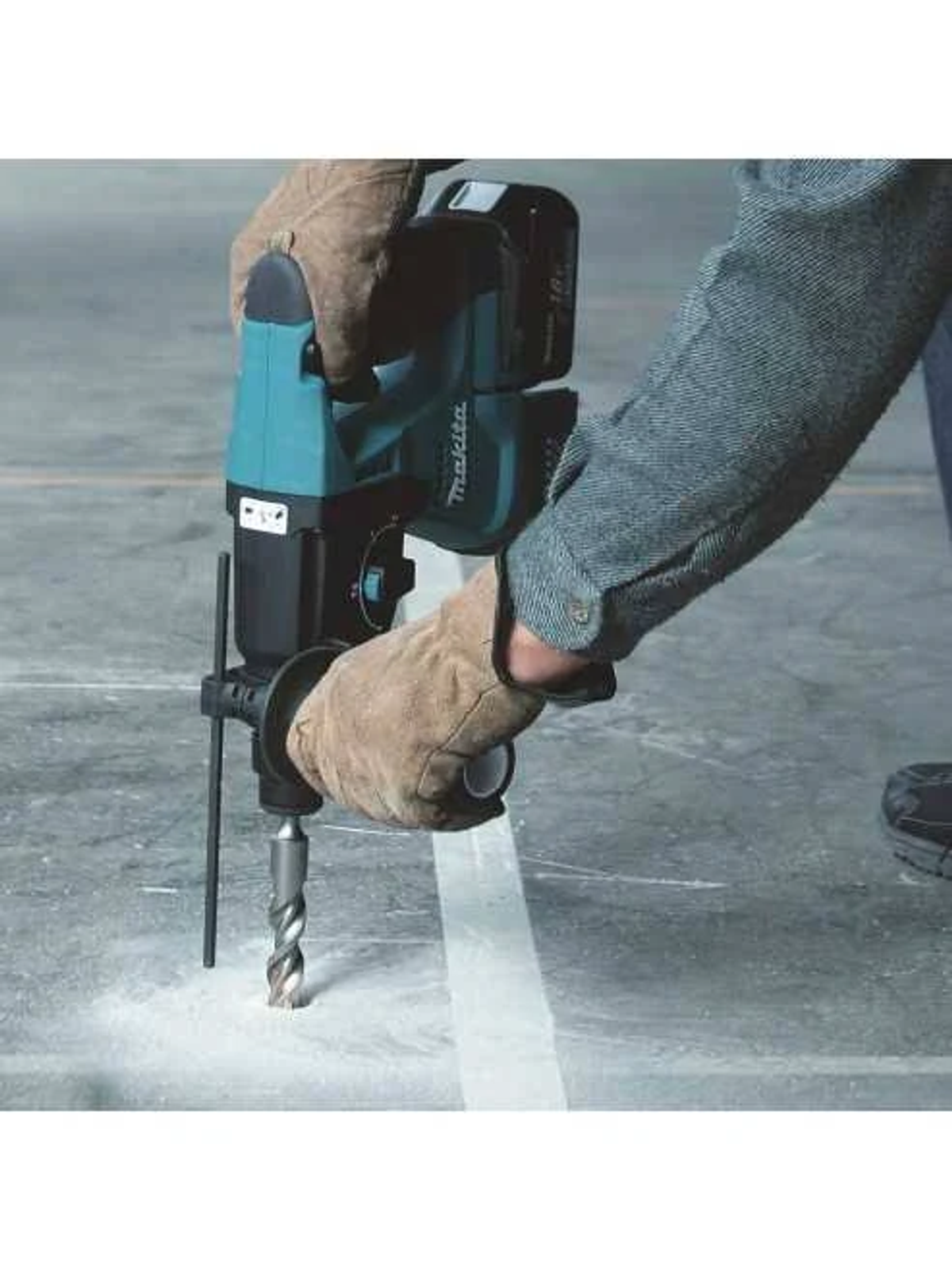 Una persona usando un taladro percutor Makita turquesa y negro sobre una superficie de concreto.