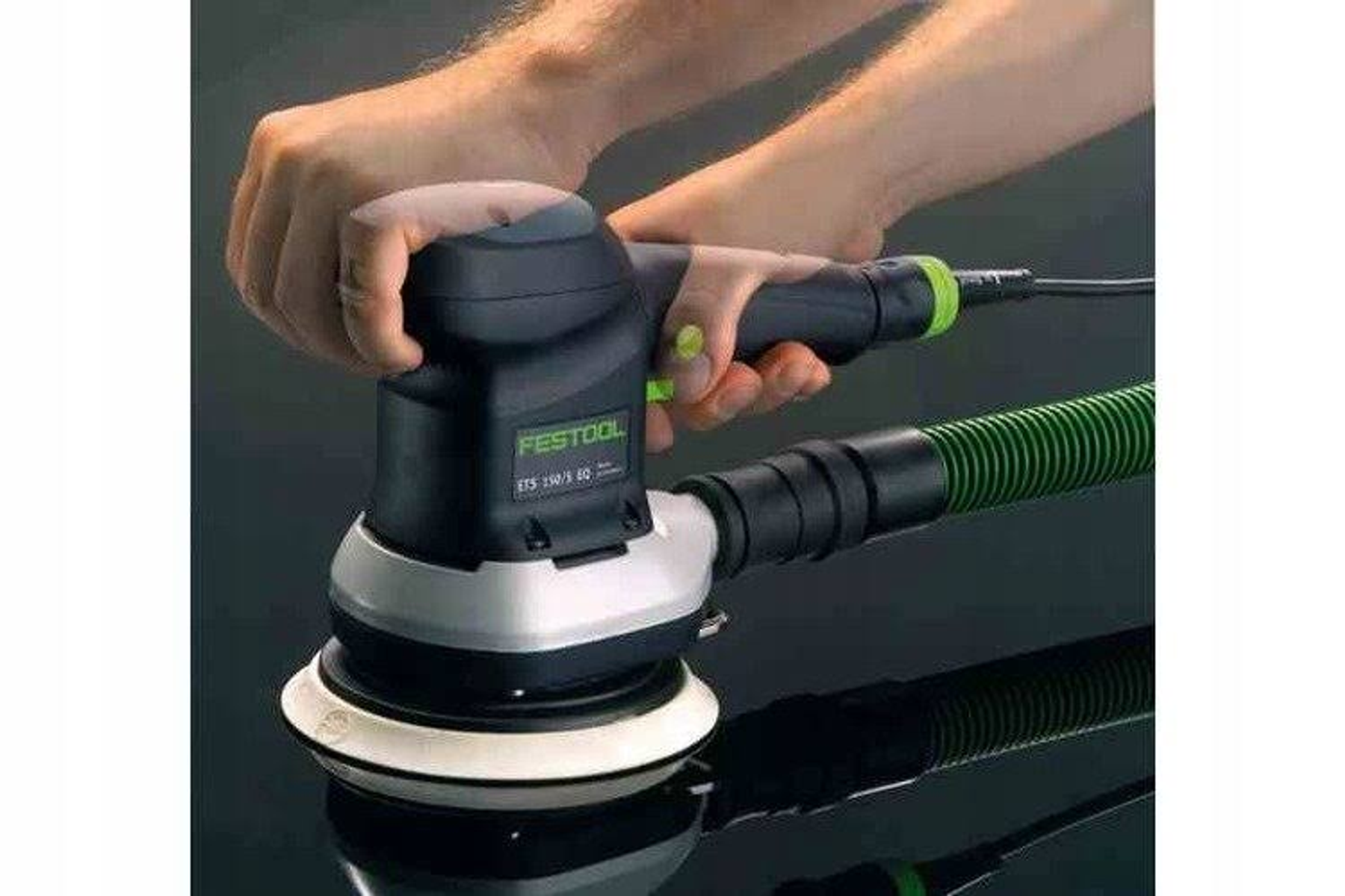 Manos sosteniendo una lijadora Festool, con una manguera y una almohadilla de lijado blanca.
