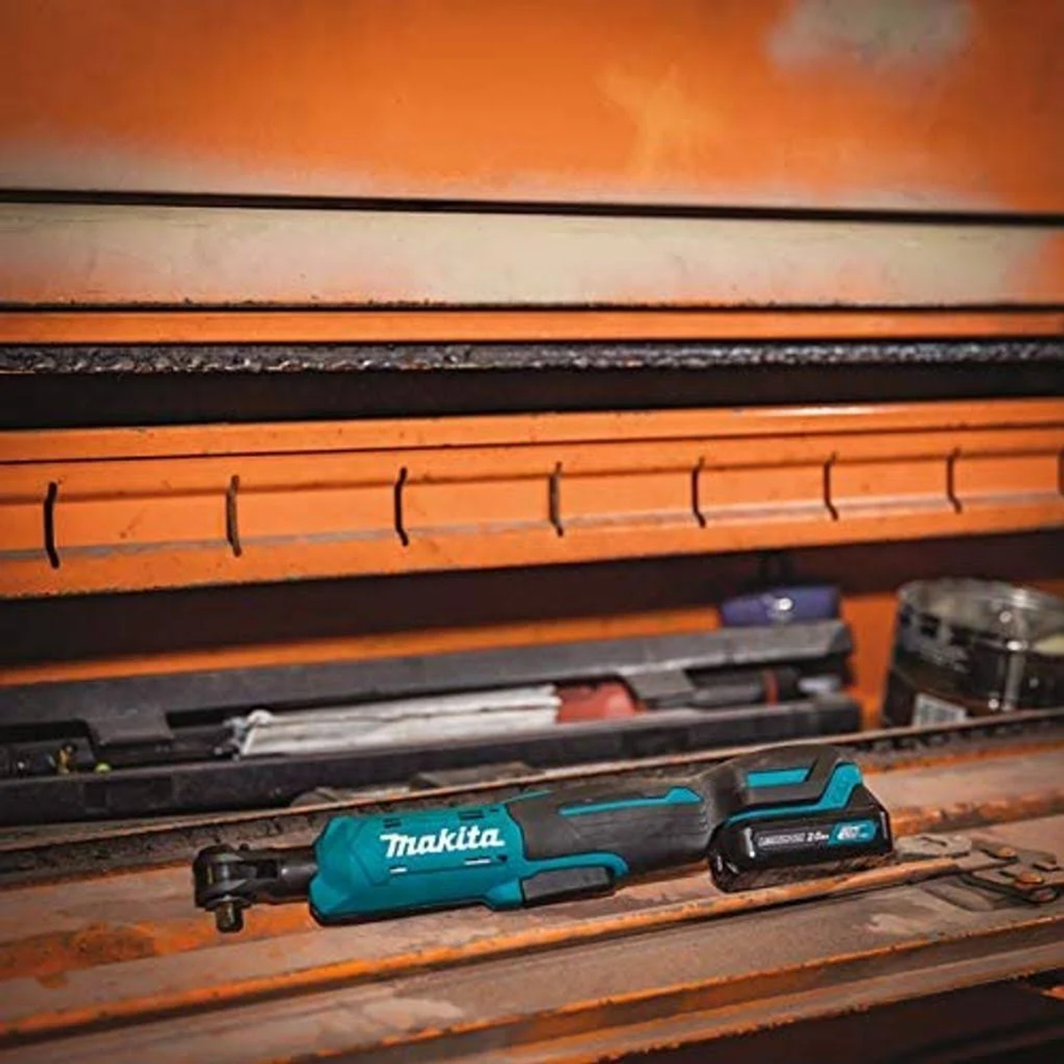 Una llave de impacto Makita turquesa y negra con una batería, colocada en una caja de herramientas naranja.