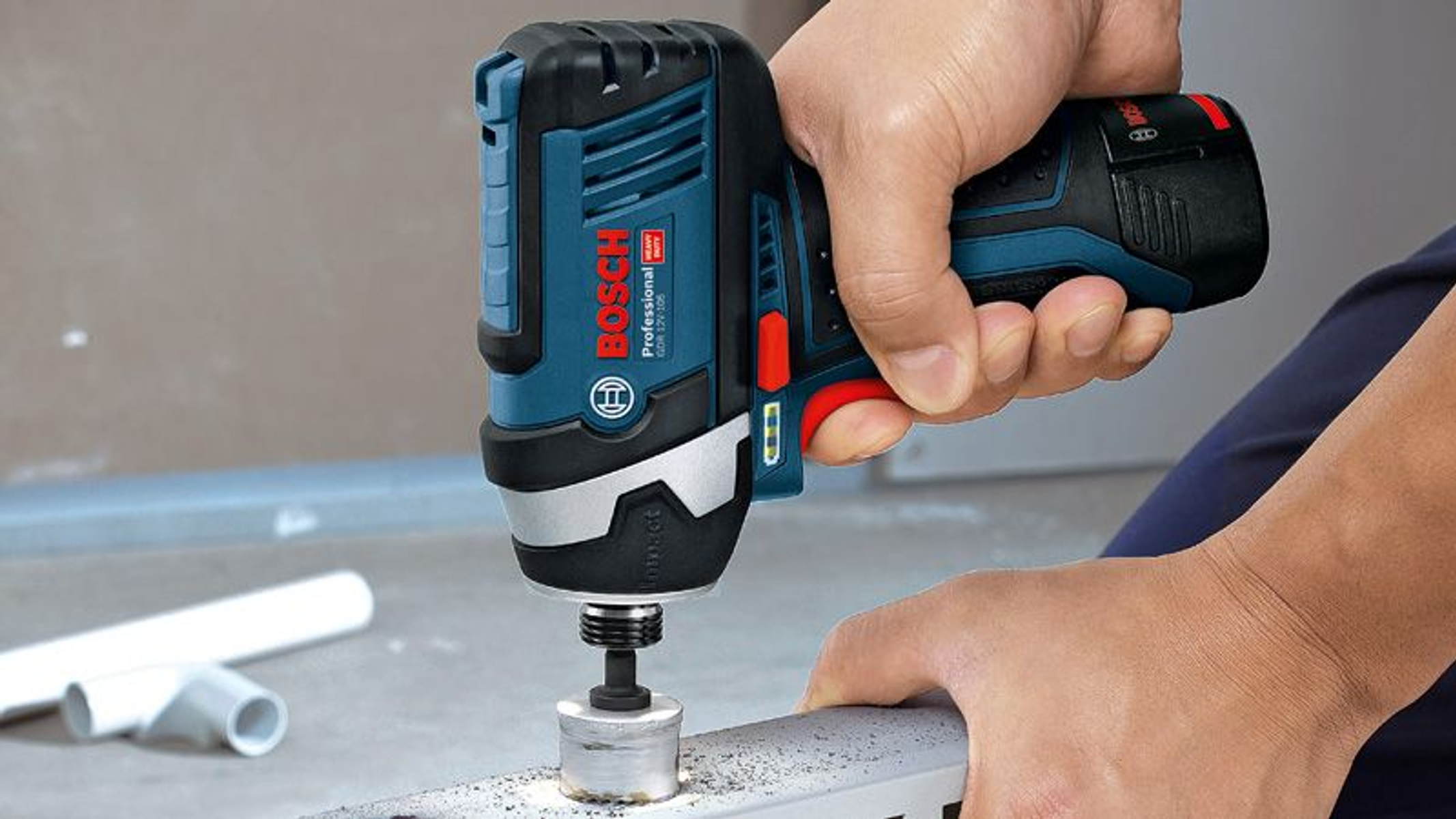 Una mano sosteniendo un taladro Bosch azul y negro, perforando una superficie metálica.