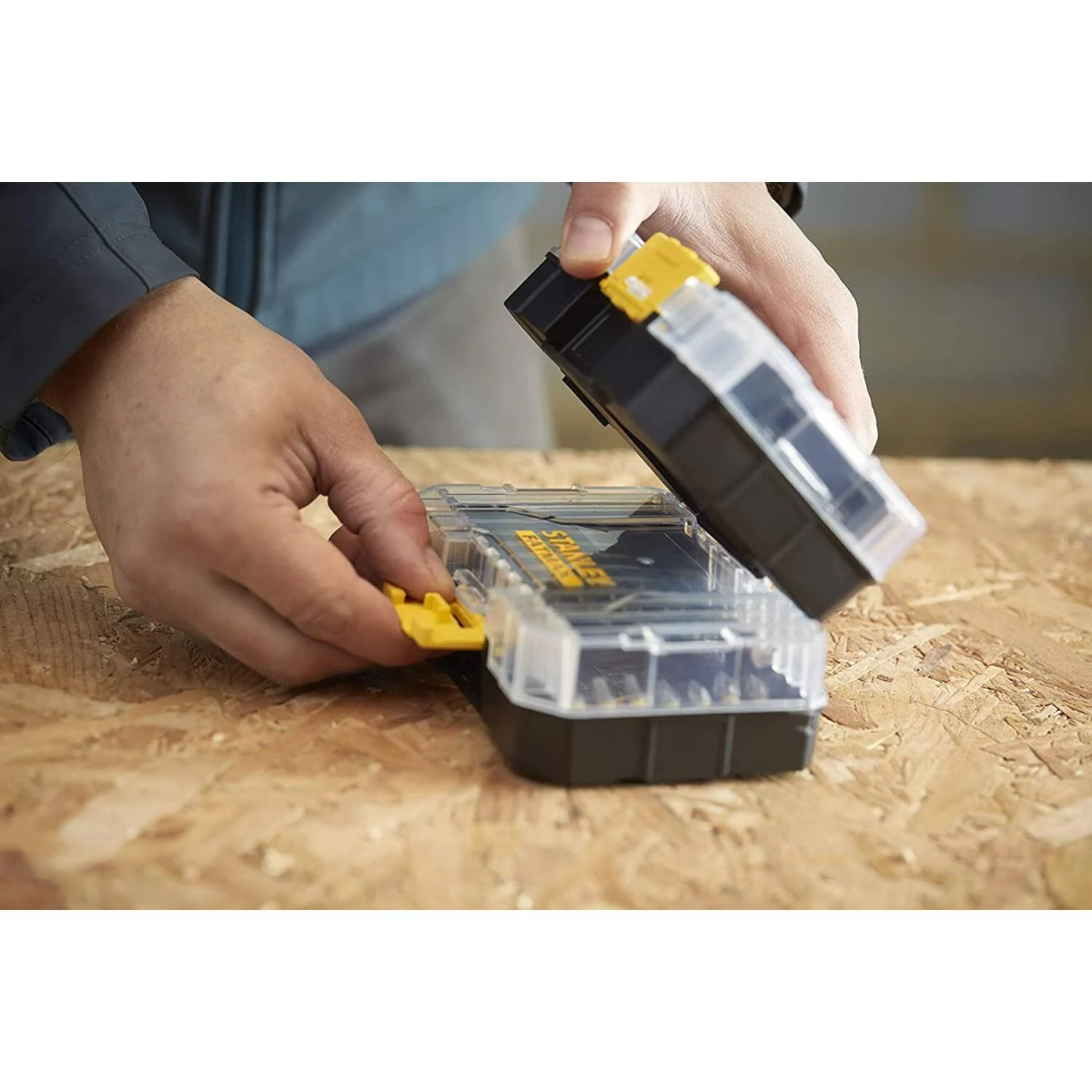 Manos abriendo una caja organizadora Stanley FatMax, revelando compartimentos y contenido.