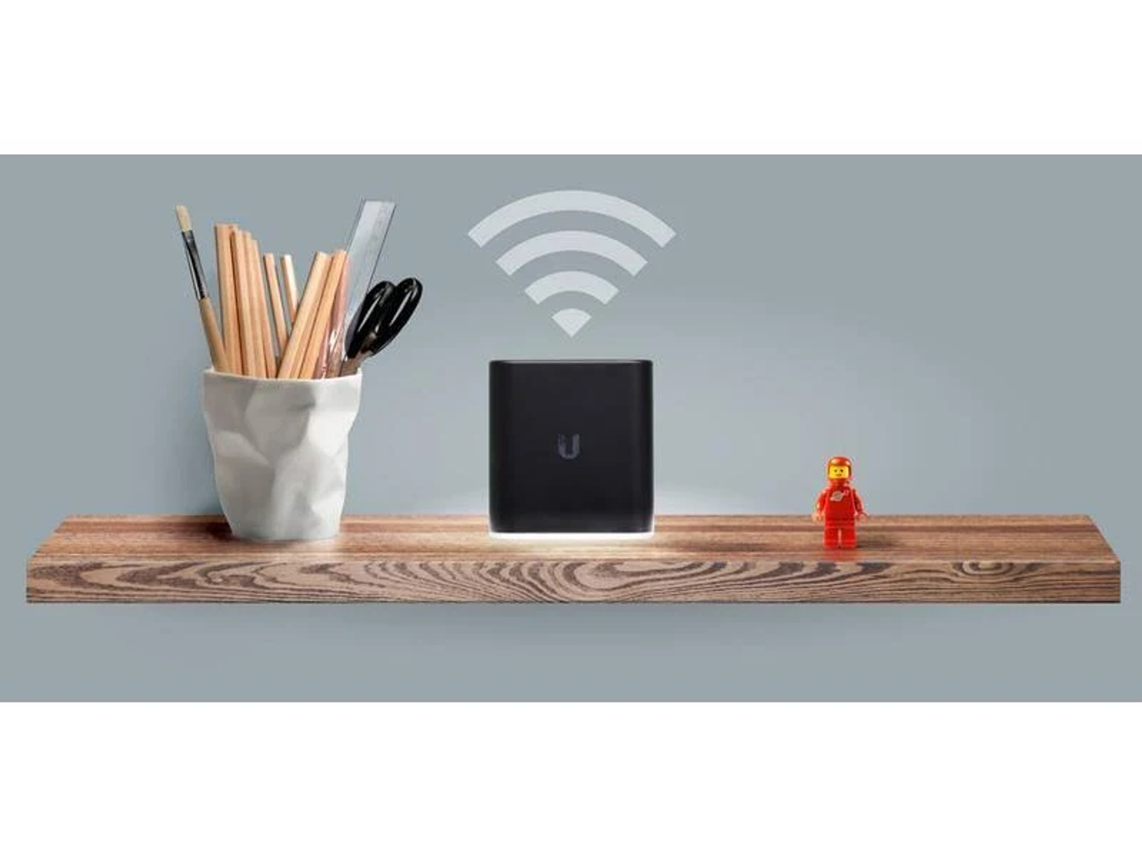 Un router nero su una mensola di legno con matite, forbici e un personaggio Lego.