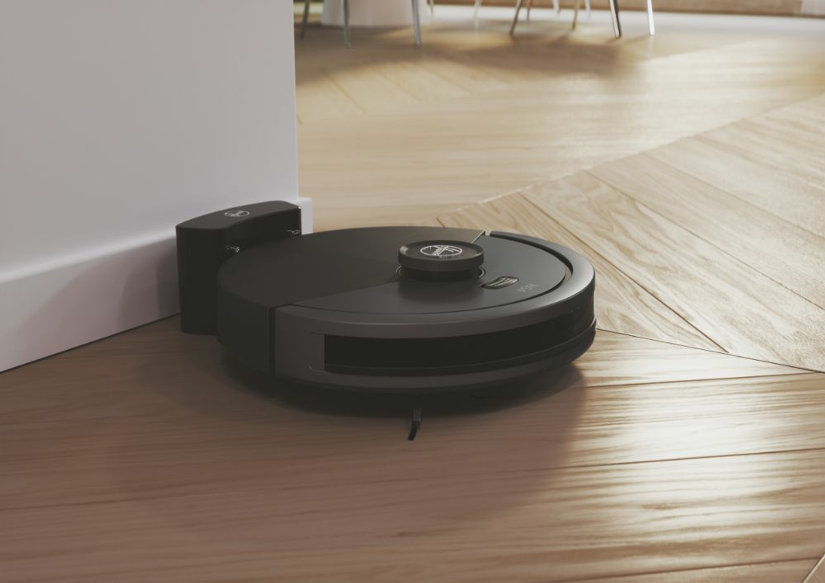 Ein dunkelgrauer Roboter-Staubsauger liegt auf einem Holzboden in der Nähe einer Wand, bereit zum Reinigen.