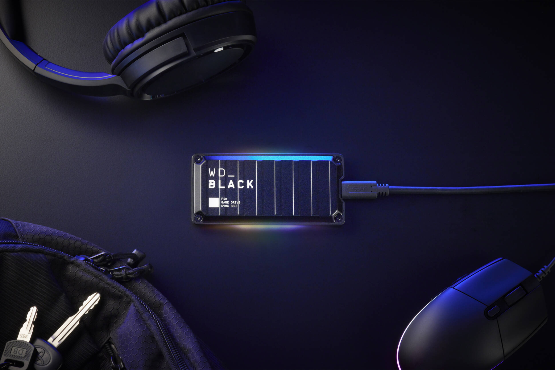 Dysk zewnętrzny WD_BLACK, czarny, ze słuchawkami, myszą, kluczami, na ciemnej powierzchni.