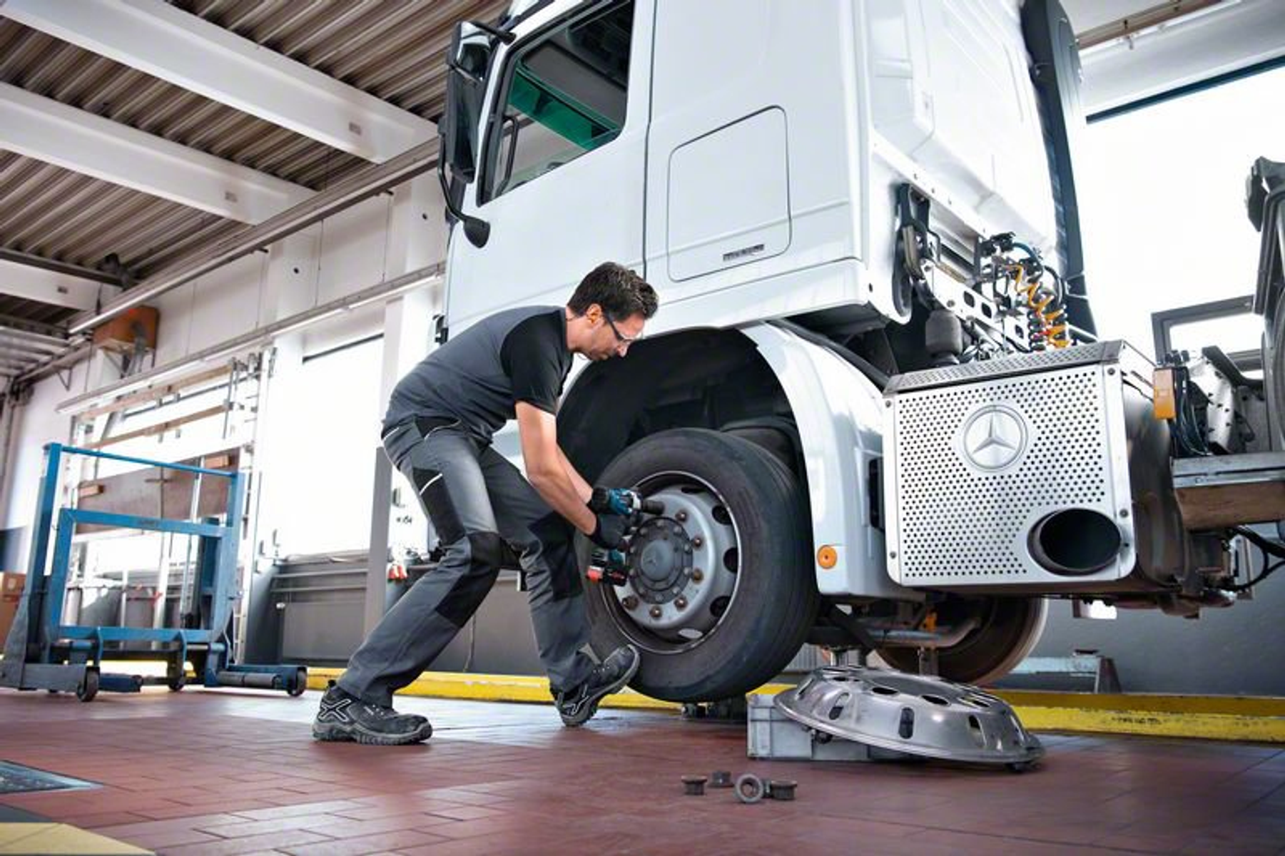 Mechanik pracuje nad oponą ciężarówki. Czerwona ceglana podłoga i biała kabina.