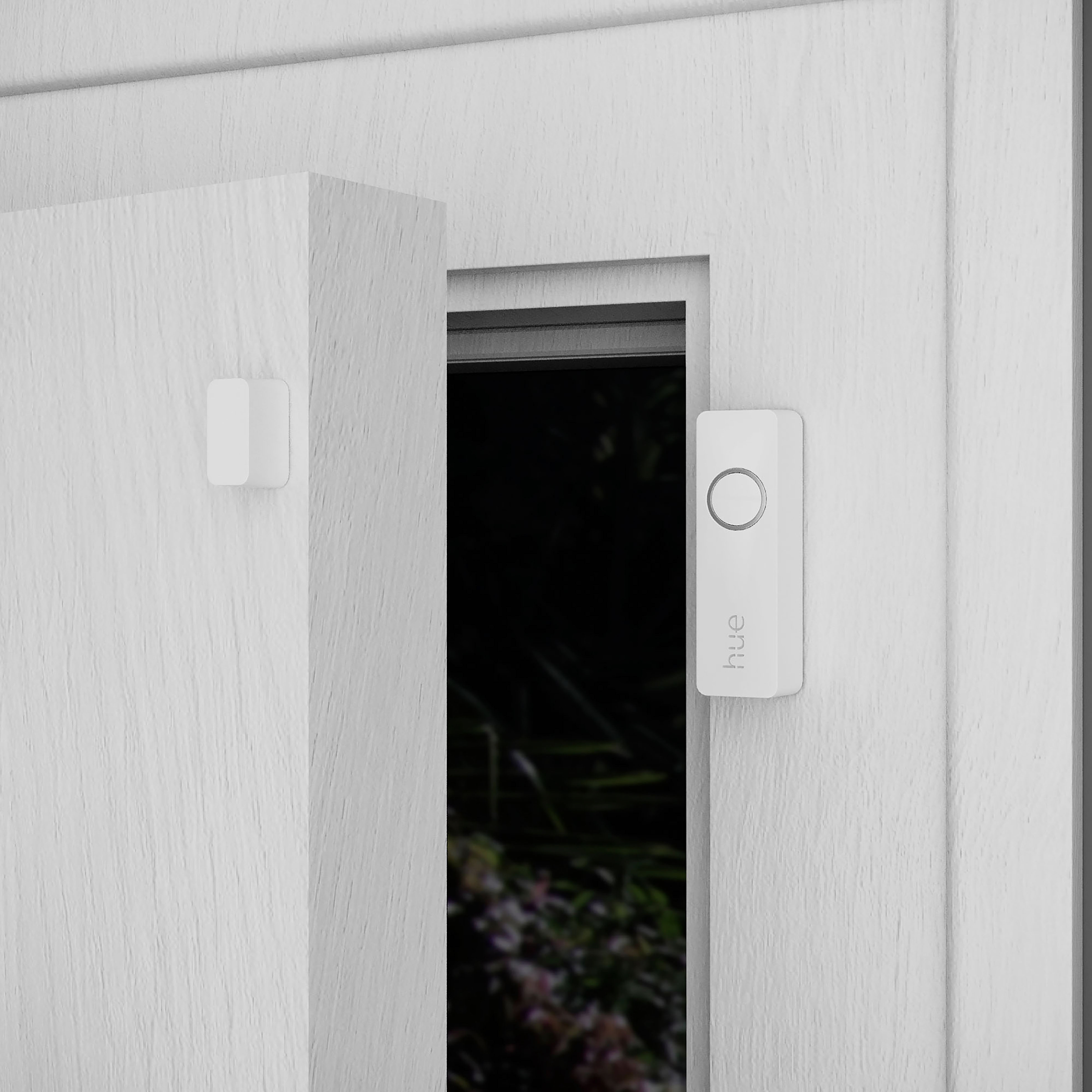 Białe drzwi i ościeżnica z małym białym urządzeniem na ścianie i białym dzwonkiem do drzwi.