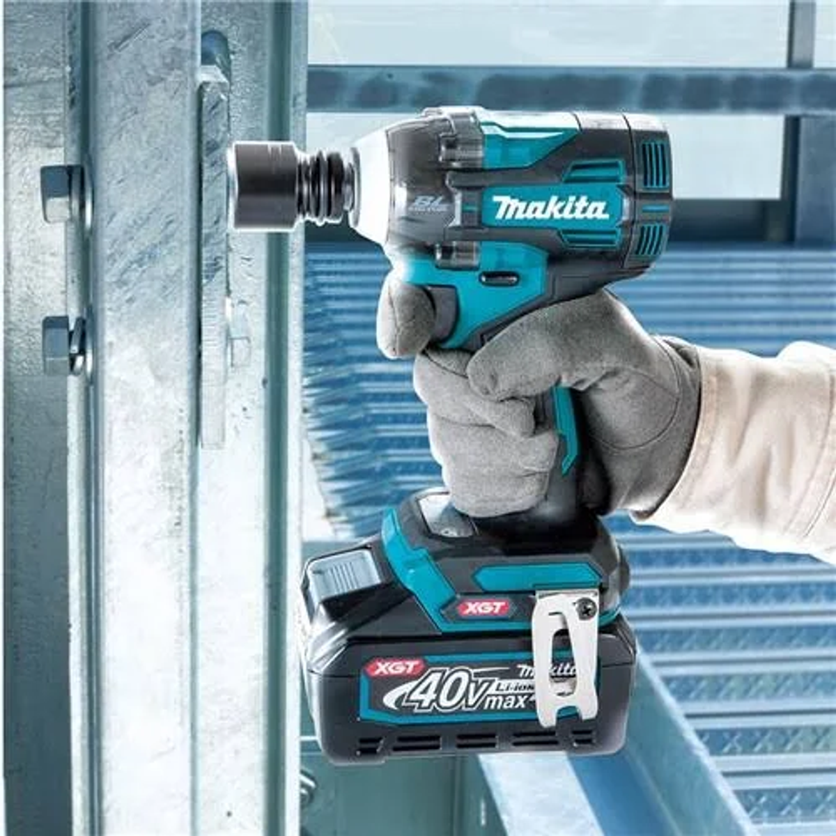 Una persona usando una llave de impacto Makita azul y negra en una estructura metálica.