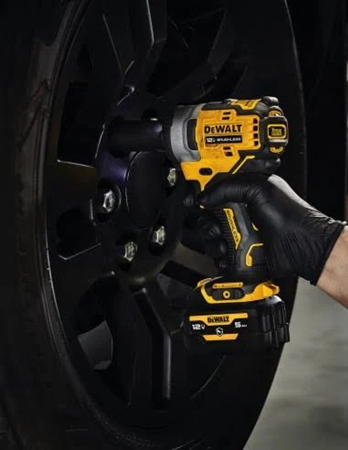 Osoba w czarnych rękawicach używająca żółto-czarnej zakrętarki udarowej DeWalt na kole.