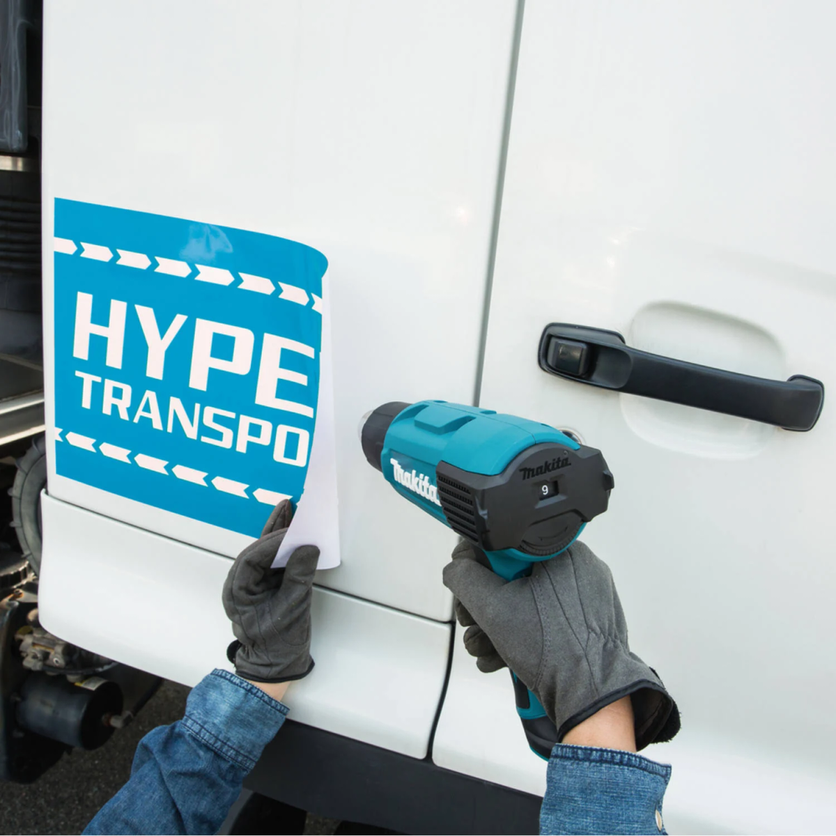 Osoba używająca turkusowo-czarnej opalarki do nakładania naklejki na bok białej ciężarówki.