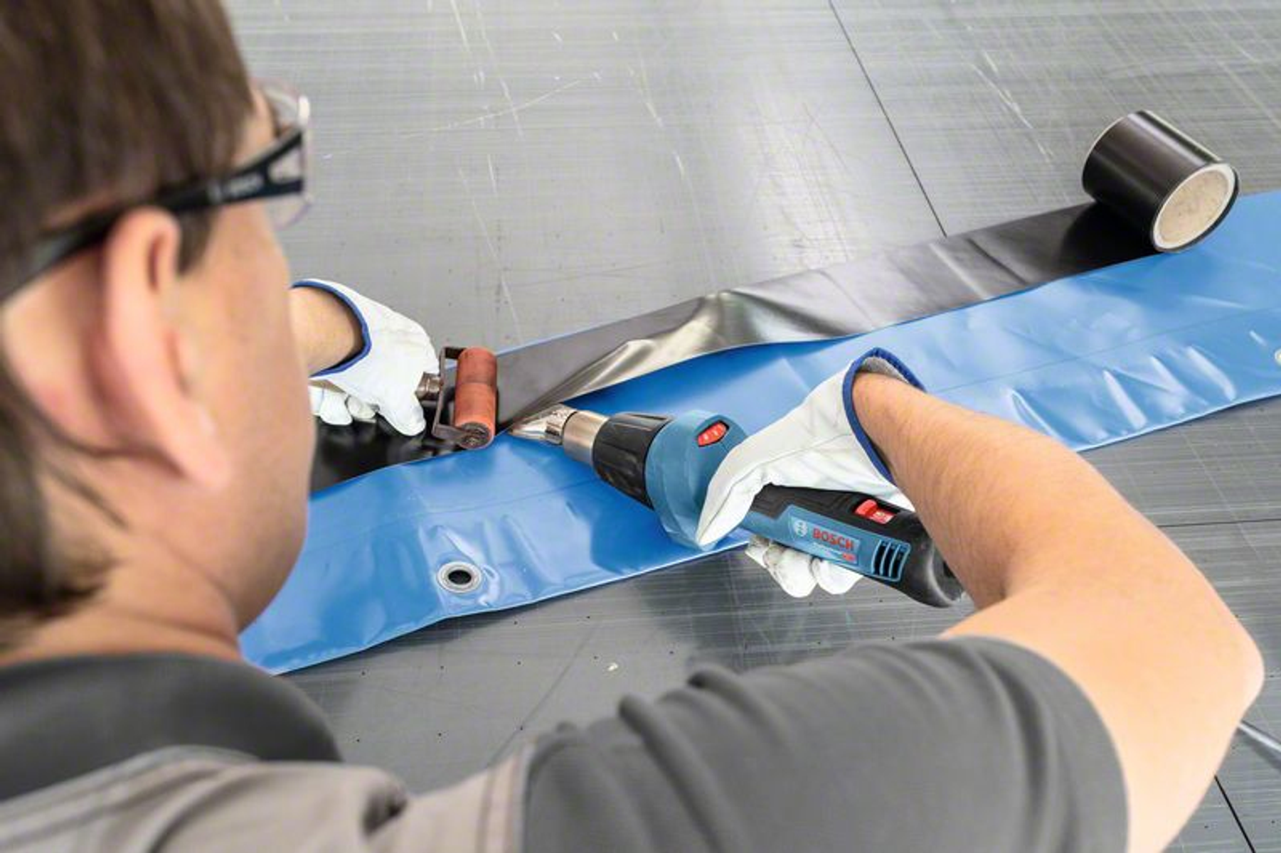 Osoba używająca opalarki do uszczelniania czarnego paska na niebieskiej plandece.