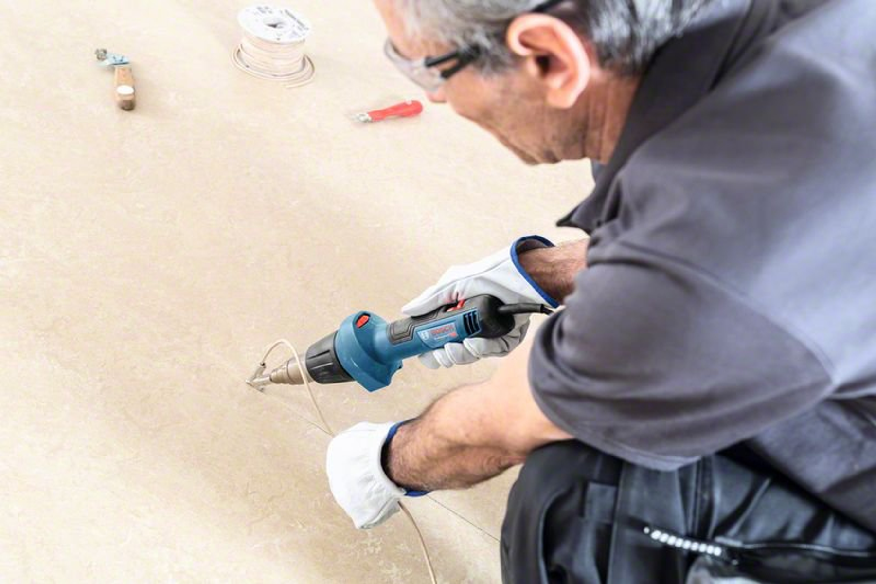 Osoba używająca niebieskiej opalarki na ścianie, widoczne narzędzia i przewody.