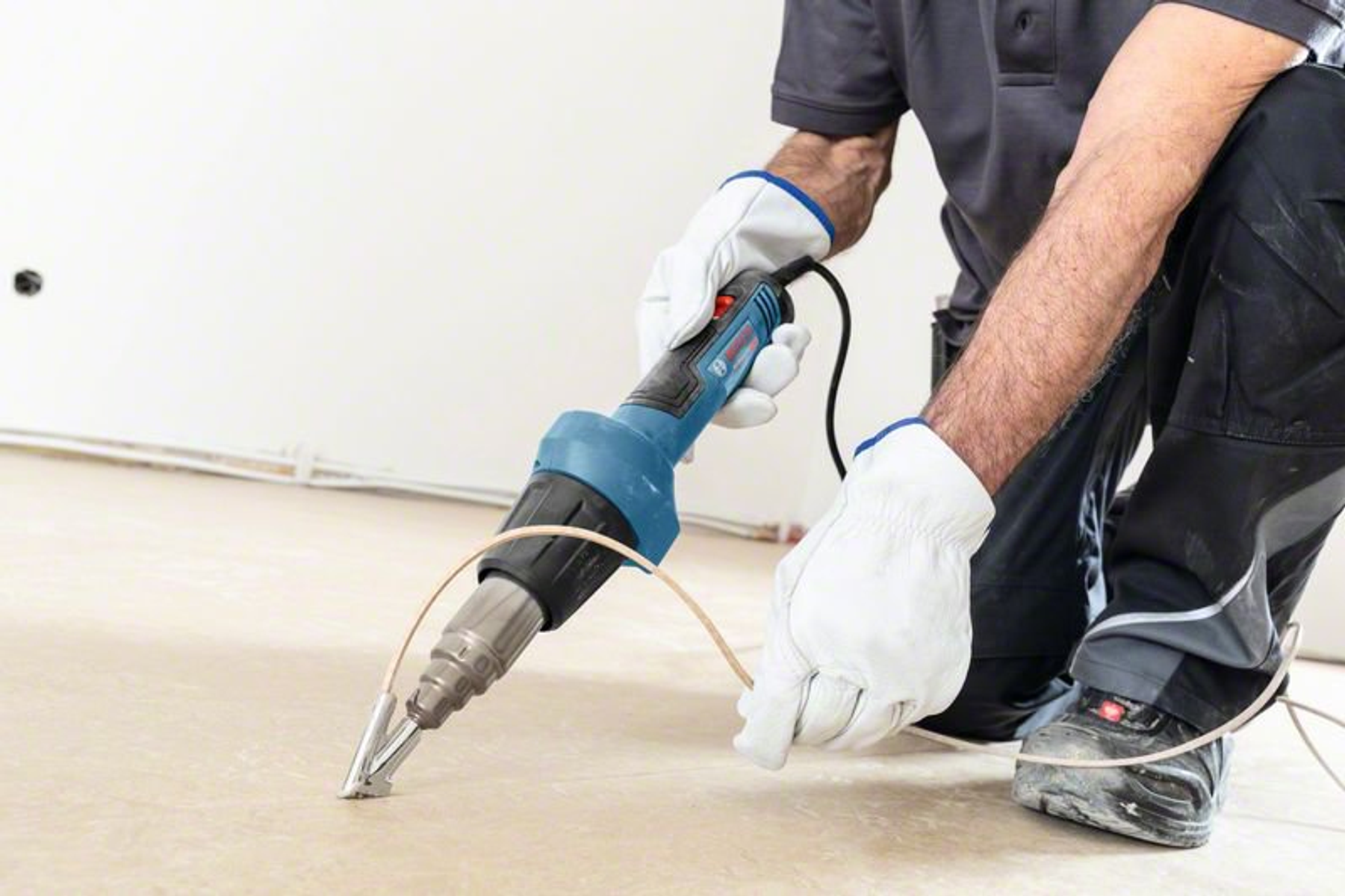 Osoba używająca niebiesko-czarnej opalarki na podłodze. Noszone są białe rękawice.