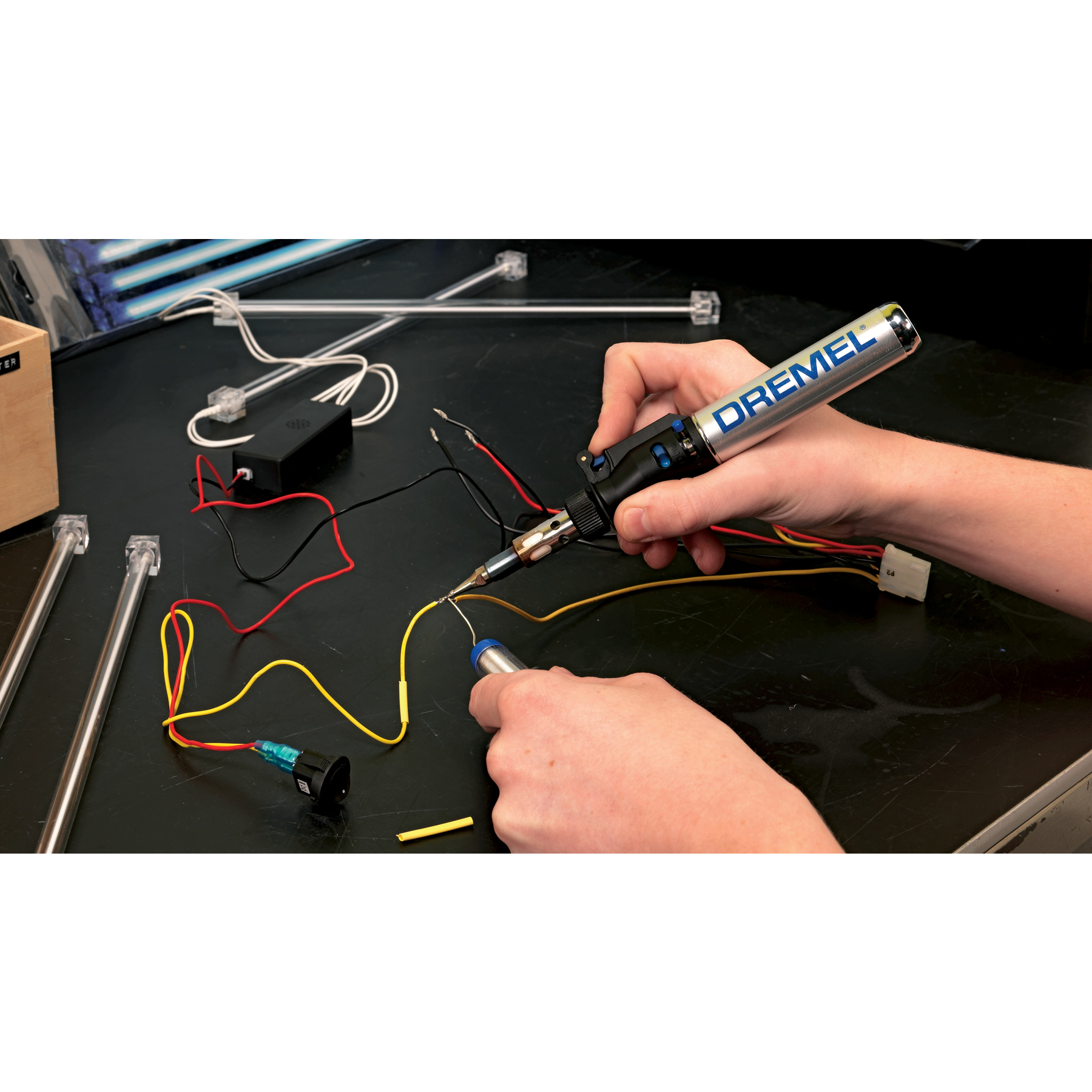 Una persona che salda fili con un saldatore Dremel, su una superficie scura.