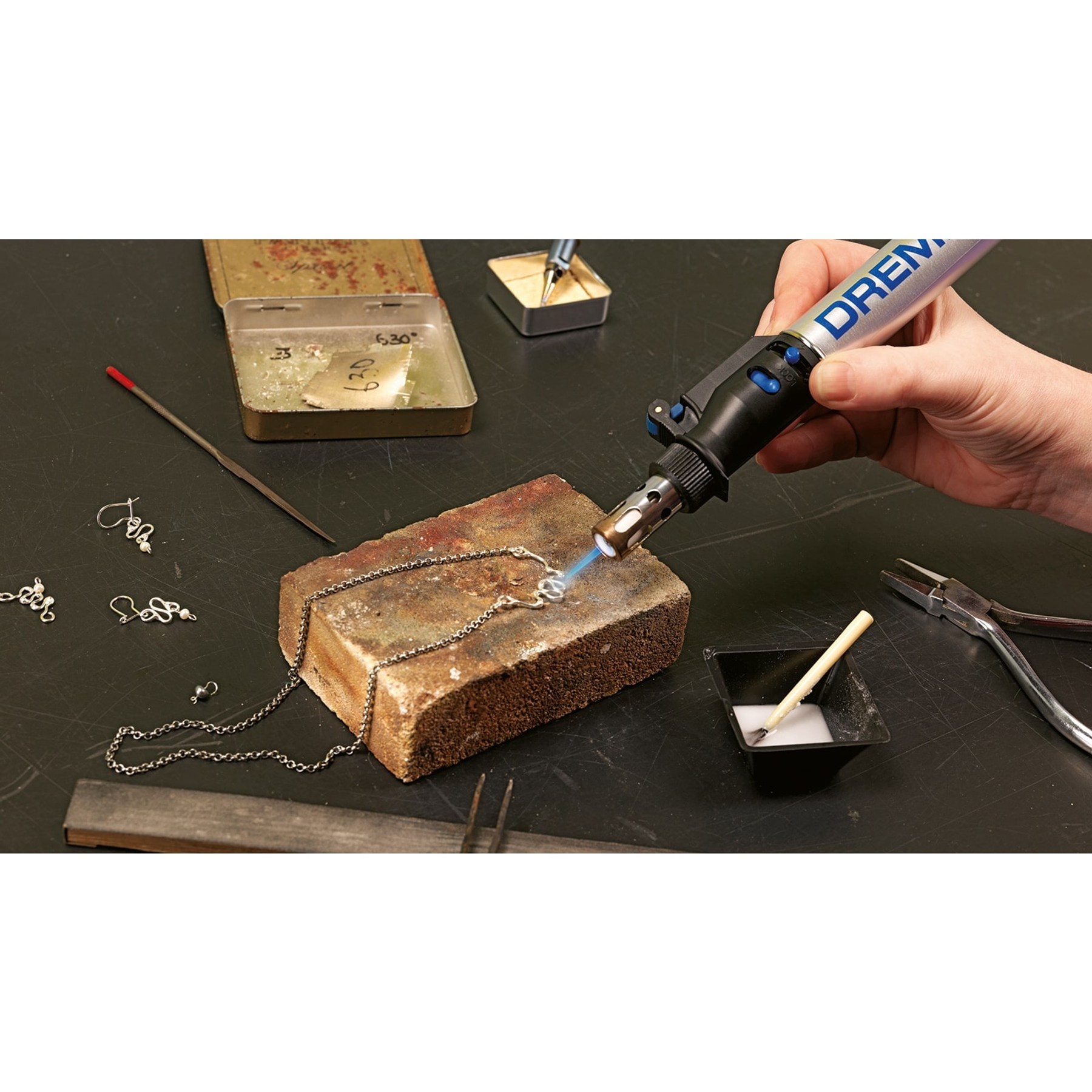 Una persona usa un utensile Dremel per saldare una collana su un mattone.