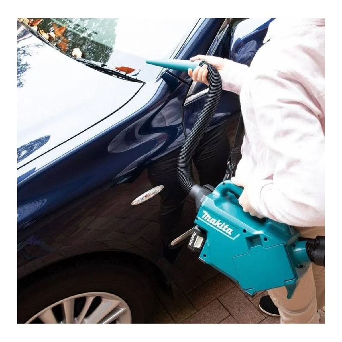 Persona che aspira un'auto. L'auto è blu scuro. L'aspirapolvere è verde acqua e nero.
