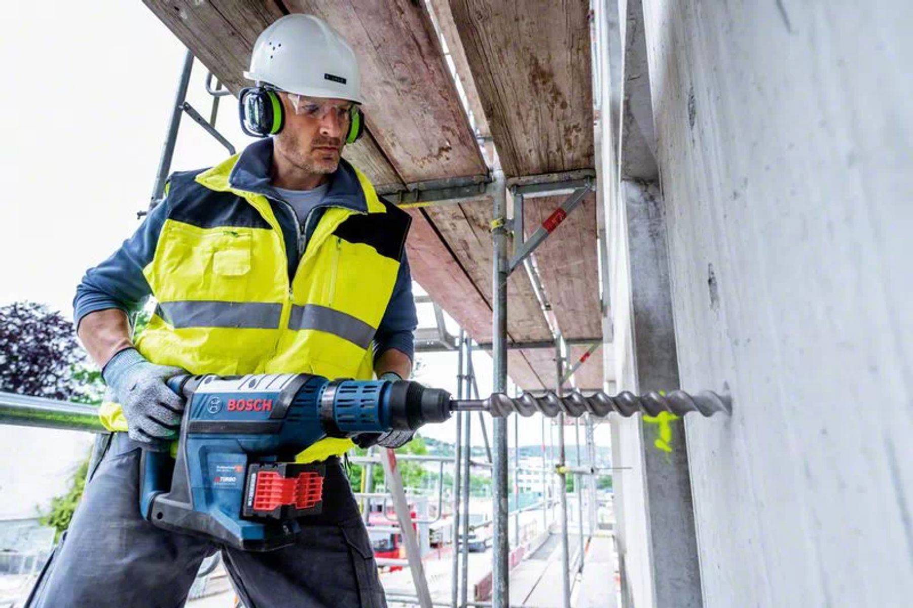 Trabajador de la construcción taladrando hormigón con taladro potente, con equipo de seguridad.