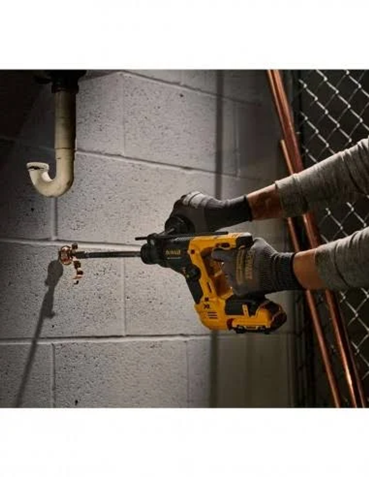 Una persona con guantes taladra una tubería cerca de una pared de ladrillo con un taladro DeWalt amarillo y negro.