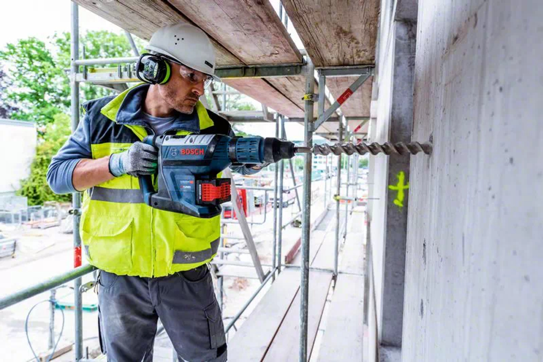 Un hombre taladrando una pared de hormigón con un martillo perforador Bosch en un andamio.