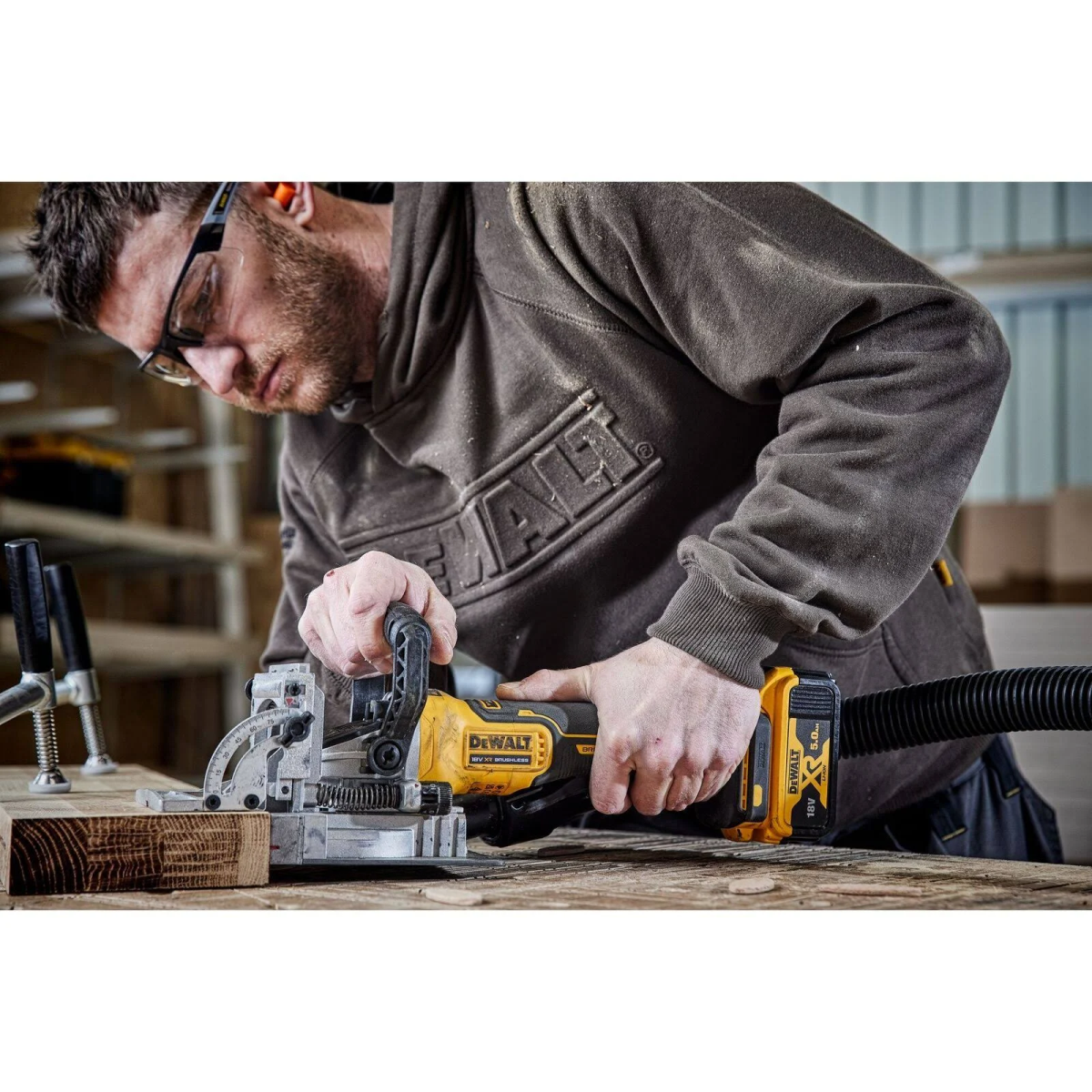 Uomo che usa un utensile DeWalt giallo e nero, con tubo aspirapolvere, che taglia il legno.