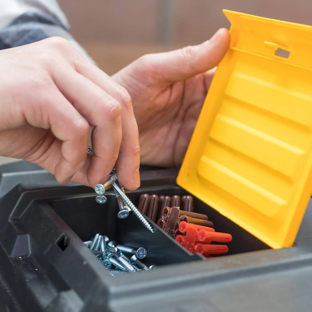 Una persona tiene viti e chiodi da una cassetta degli attrezzi nera con coperchio giallo.