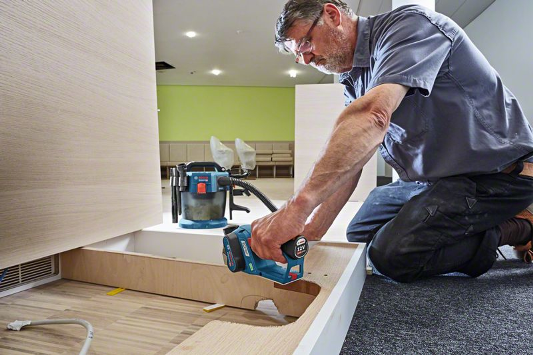 Mężczyzna używający niebiesko-czarnego elektronarzędzia, prawdopodobnie szlifierki, na drewnianej powierzchni.