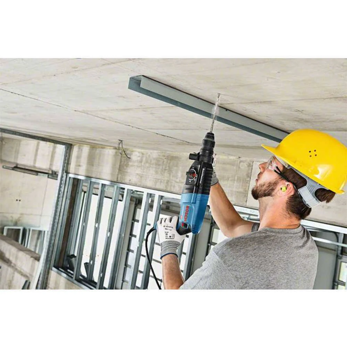 Uomo che usa un trapano, che fora un soffitto di cemento.