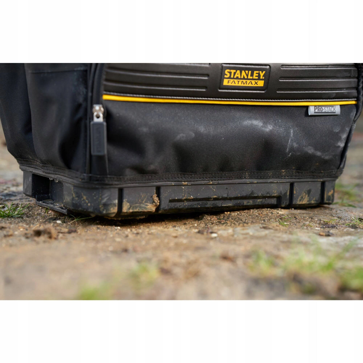 Zwarte Stanley FatMax gereedschapstas op modderige grond, close-up van de basis.