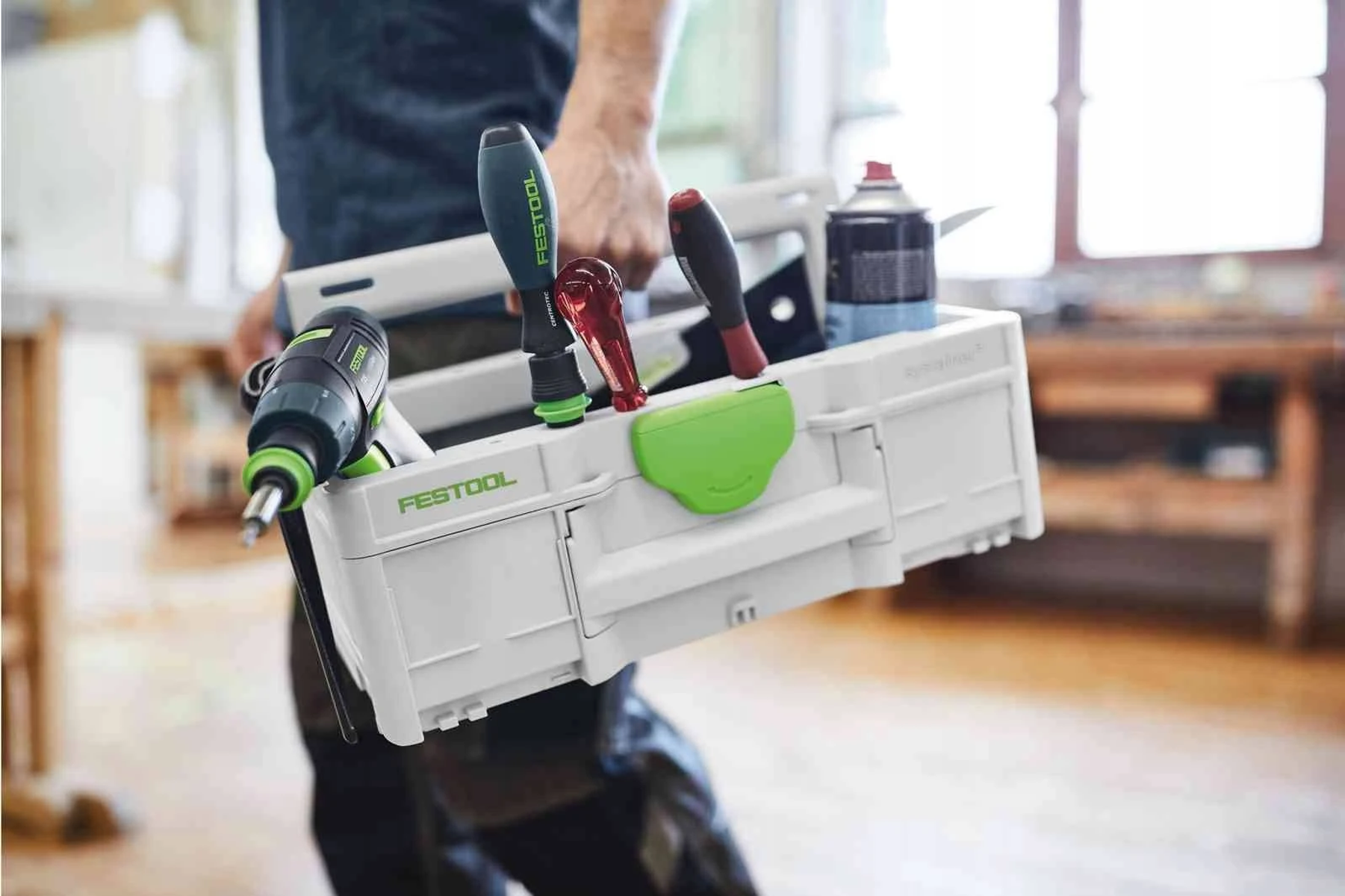 Una persona che tiene una cassetta degli attrezzi Festool bianca con attrezzi all'interno. La cassetta ha un manico verde.