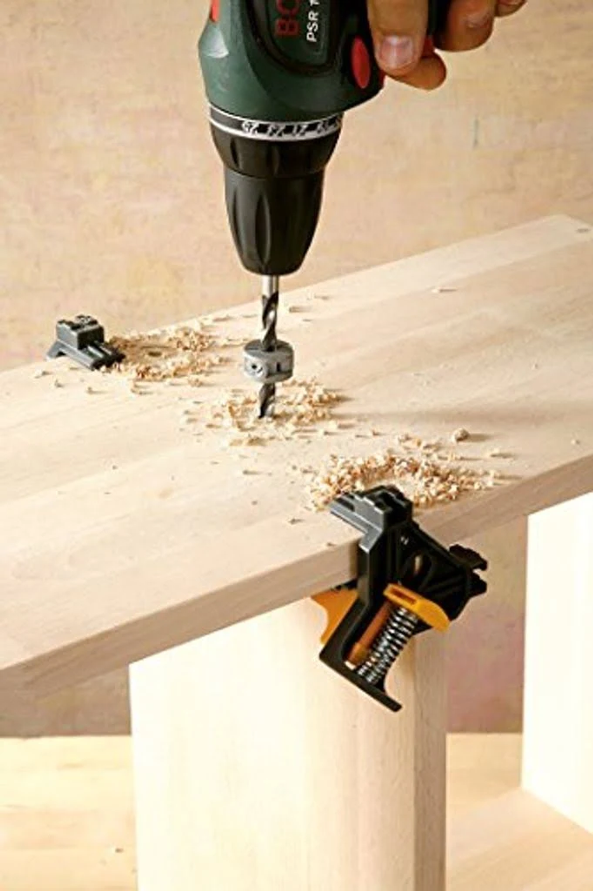 Un taladro perfora una superficie de madera. Dos abrazaderas negras aseguran la madera a la estructura.