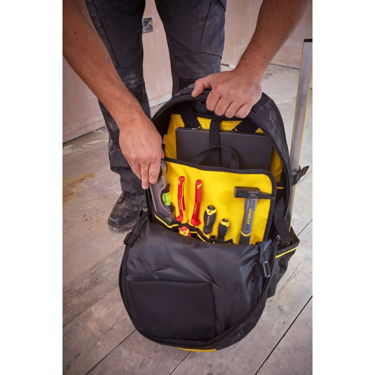 Una persona apre uno zaino Stanley nero e giallo. Utensili all'interno della borsa aperta.