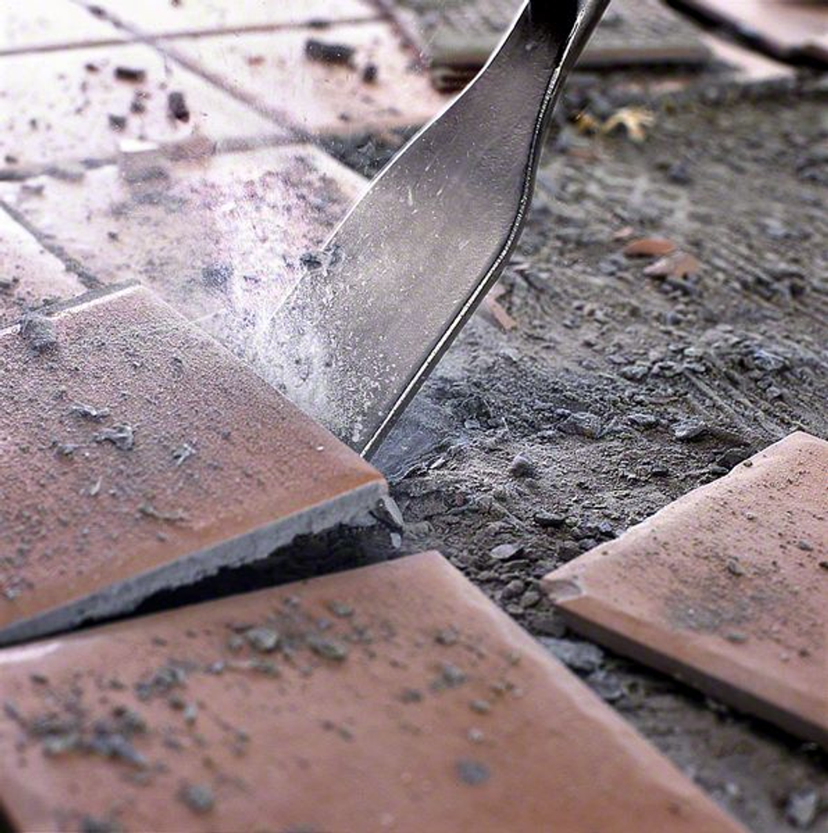 Cincel rompiendo baldosas. Baldosas marrones y concreto gris al fondo.