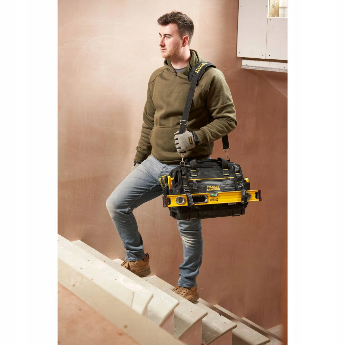 Uomo in jeans e felpa verde sale le scale con una borsa degli attrezzi.