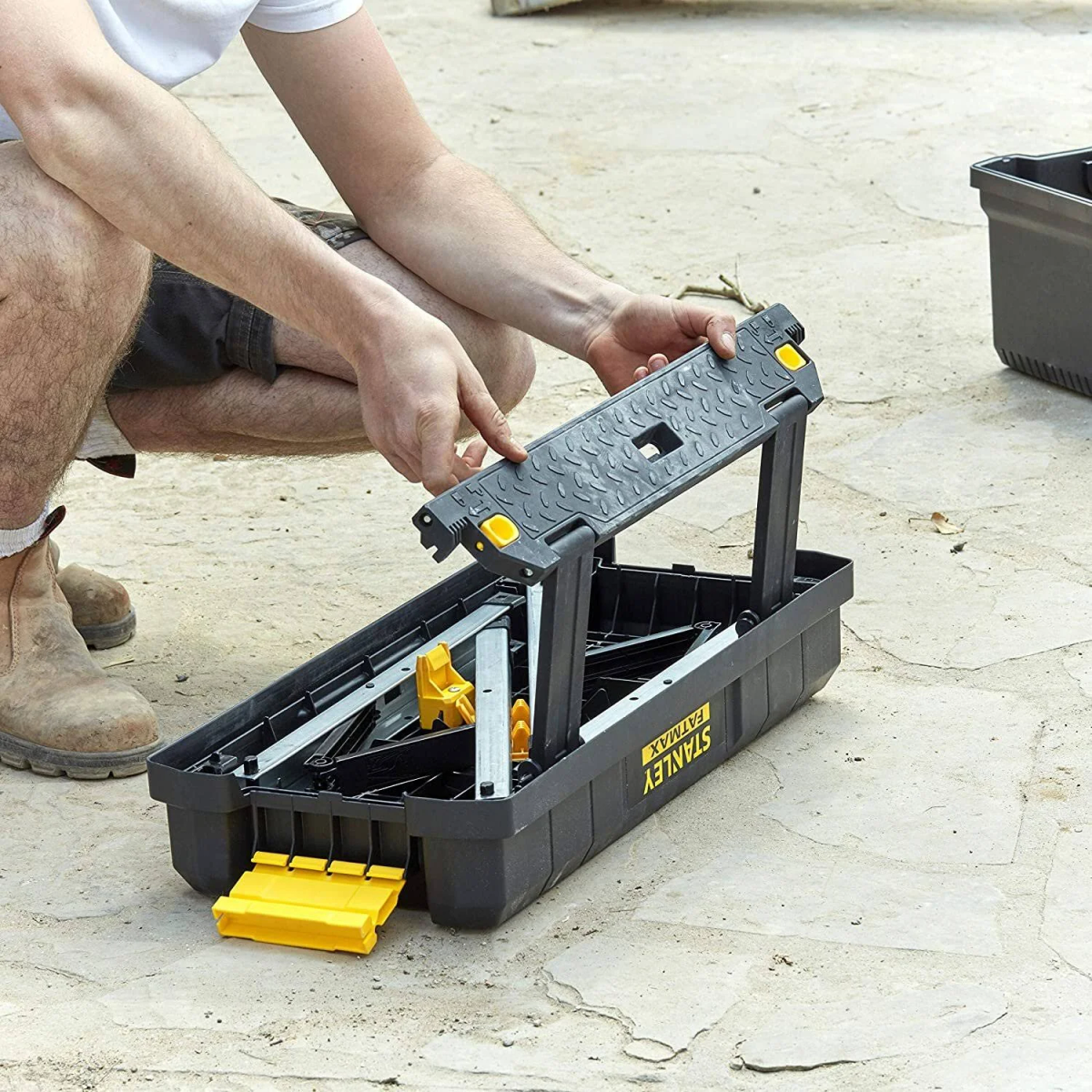Un uomo assembla una cassetta degli attrezzi Stanley FatMax nera e gialla su una superficie di cemento.